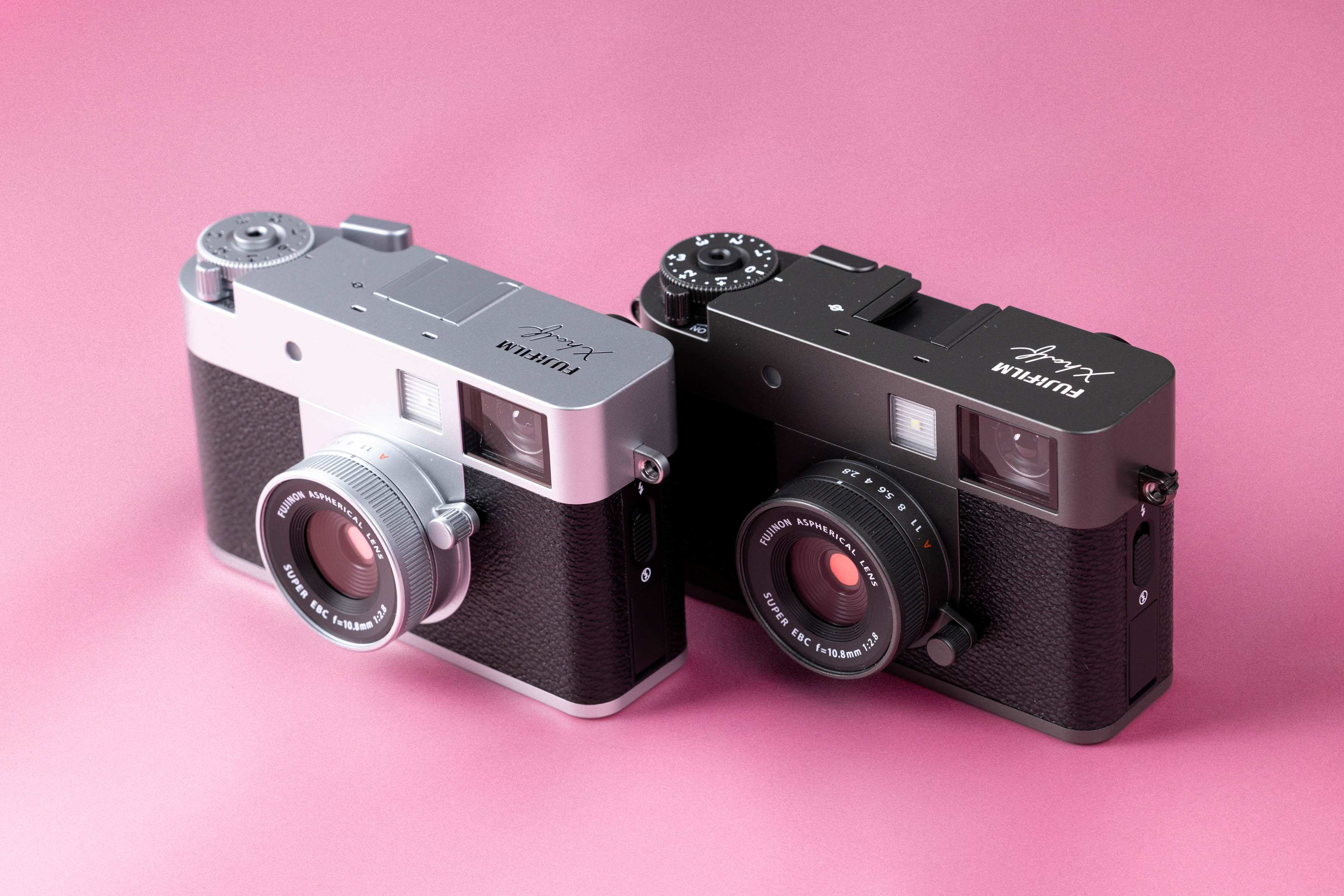 Two Fujifilm X half cameras on a soft pink background.