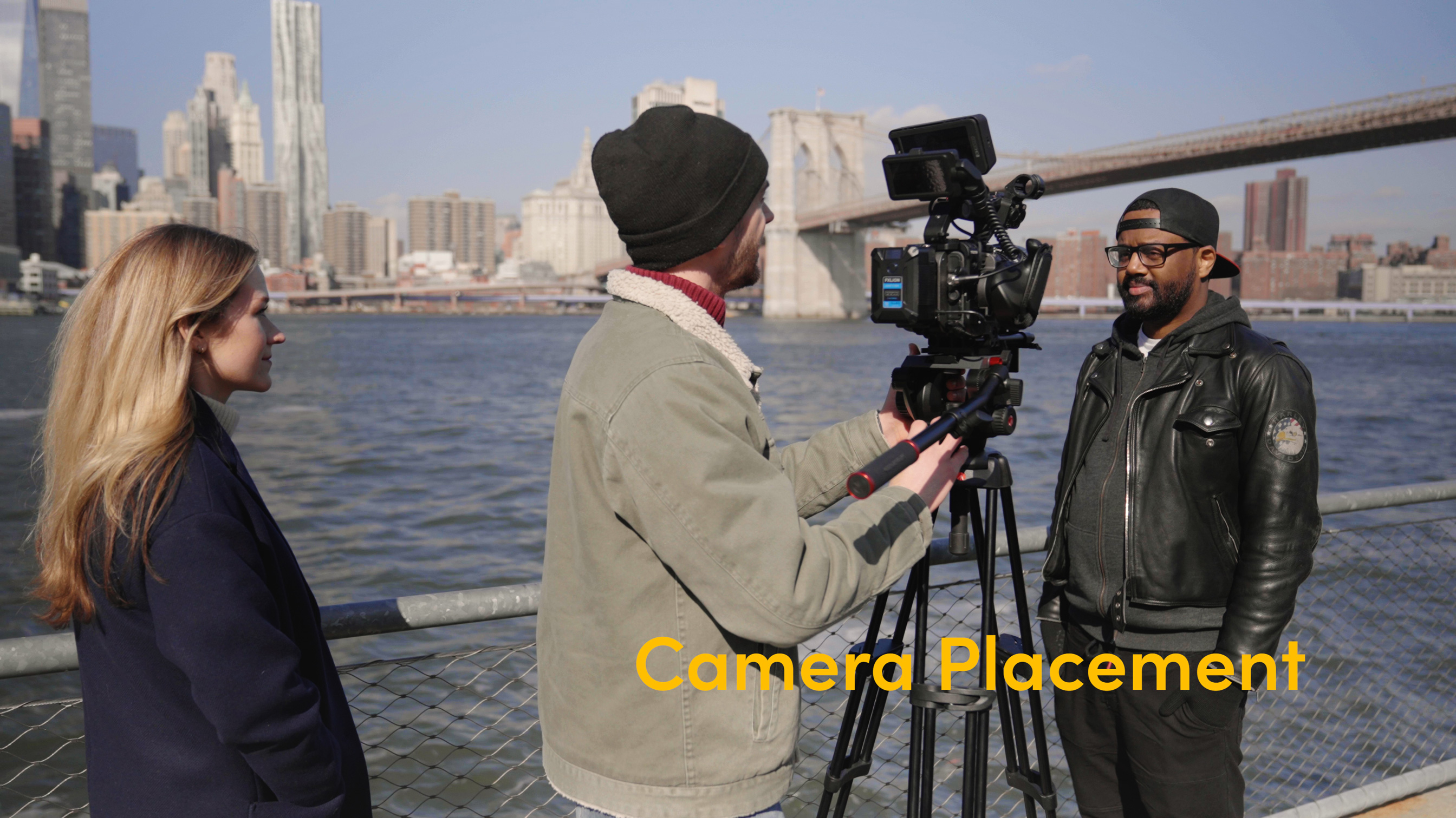 Foto van drie mensen met een camera voor het water in New York City met de Brooklyn Bridge op de achtergrond