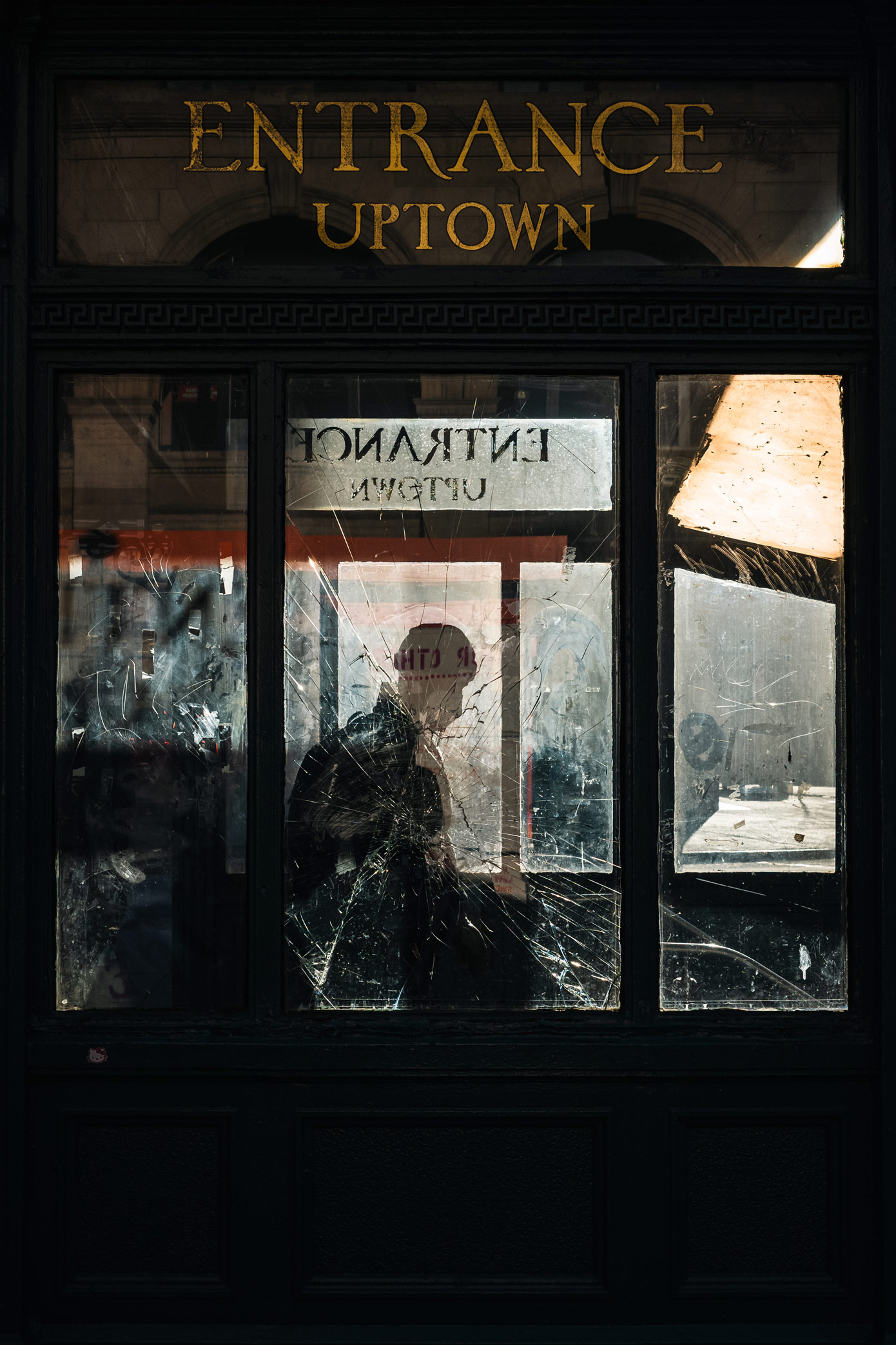 Silhouet van persoon die de NYC metro binnengaat achter een ruit van gebroken glas, gefotografeerd door Manuel Pena.