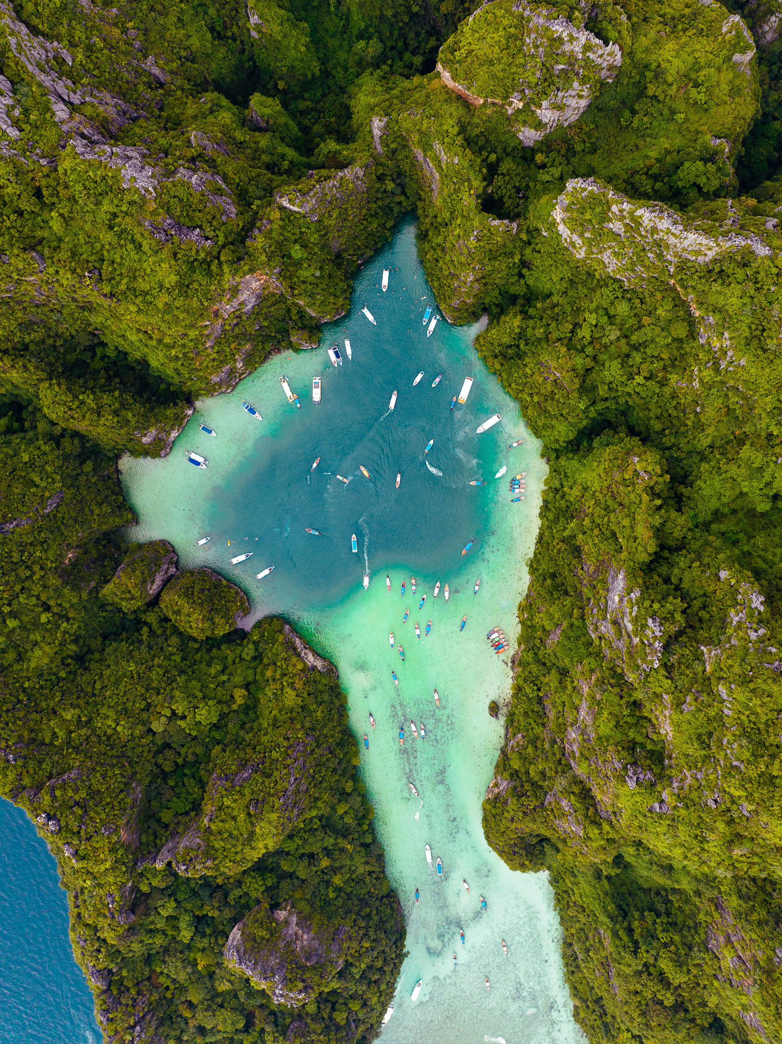Drone aerial photo of a tropical lagoon with clear turquoise water, boats, and lush green limestone cliffs.