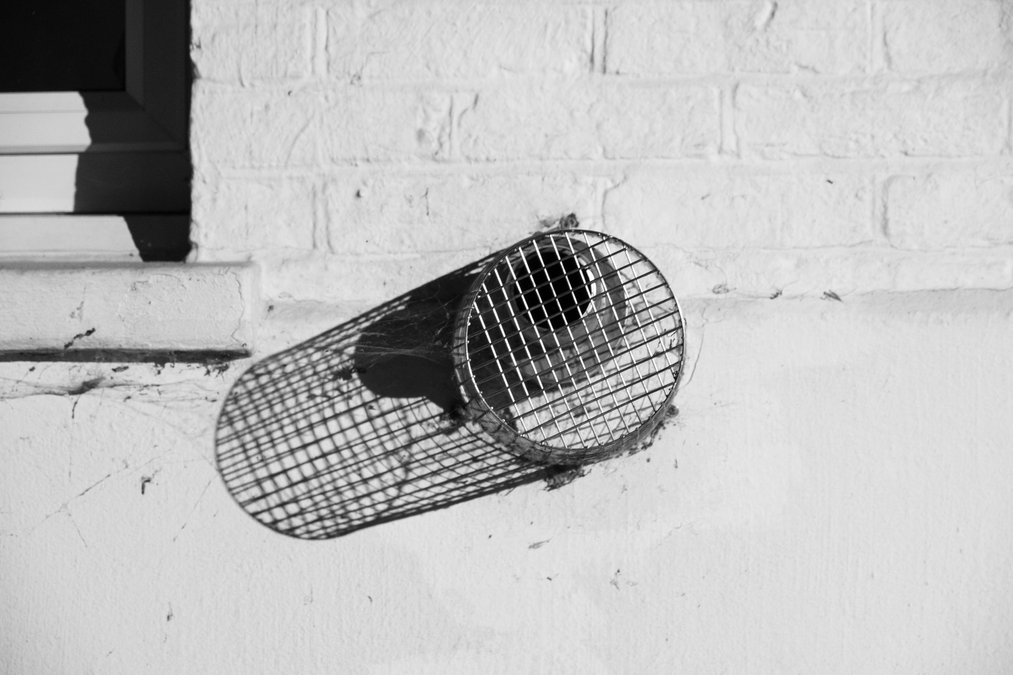 Black and white image of a small vent on a wall with metal wiring around it.