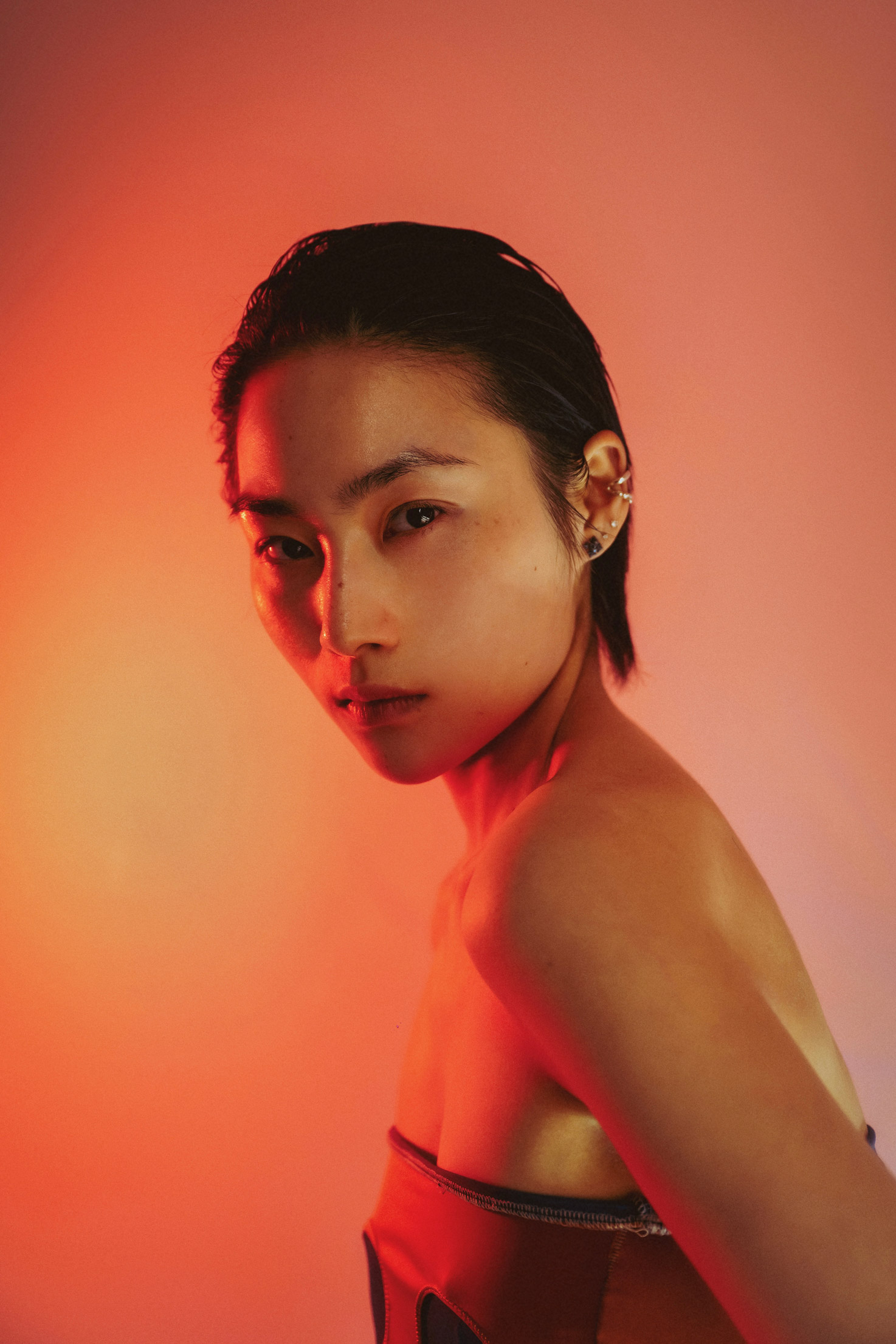 Person in front of pink and orange backdrop with a red light looking at camera, photo by Brandon Woelfel