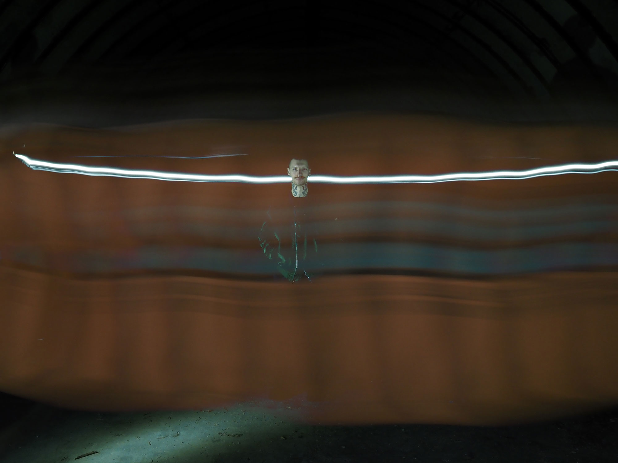 Lightpainting: Dunkel gekleidete Person in der Mitte eines dunklen Bildes mit weißem Leuchtstreifen, der hinter dem Kopf der Person vorbeiführt, aufgenommen mit einer Olympus OM-D E-M5 Mark III im Bulb-Modus