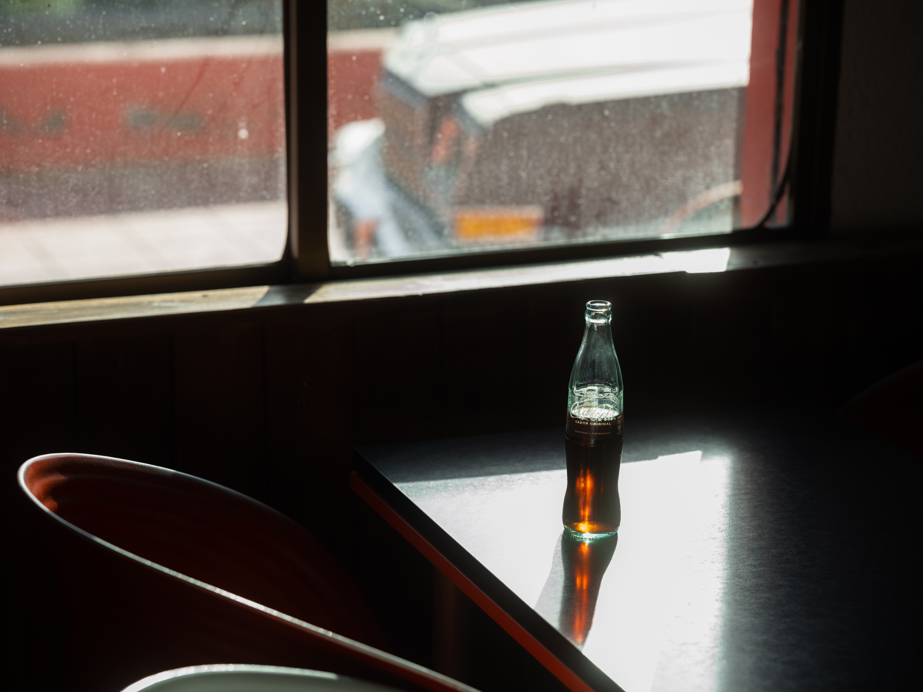 Coco-cola bottle half full on a table in the sunlight.