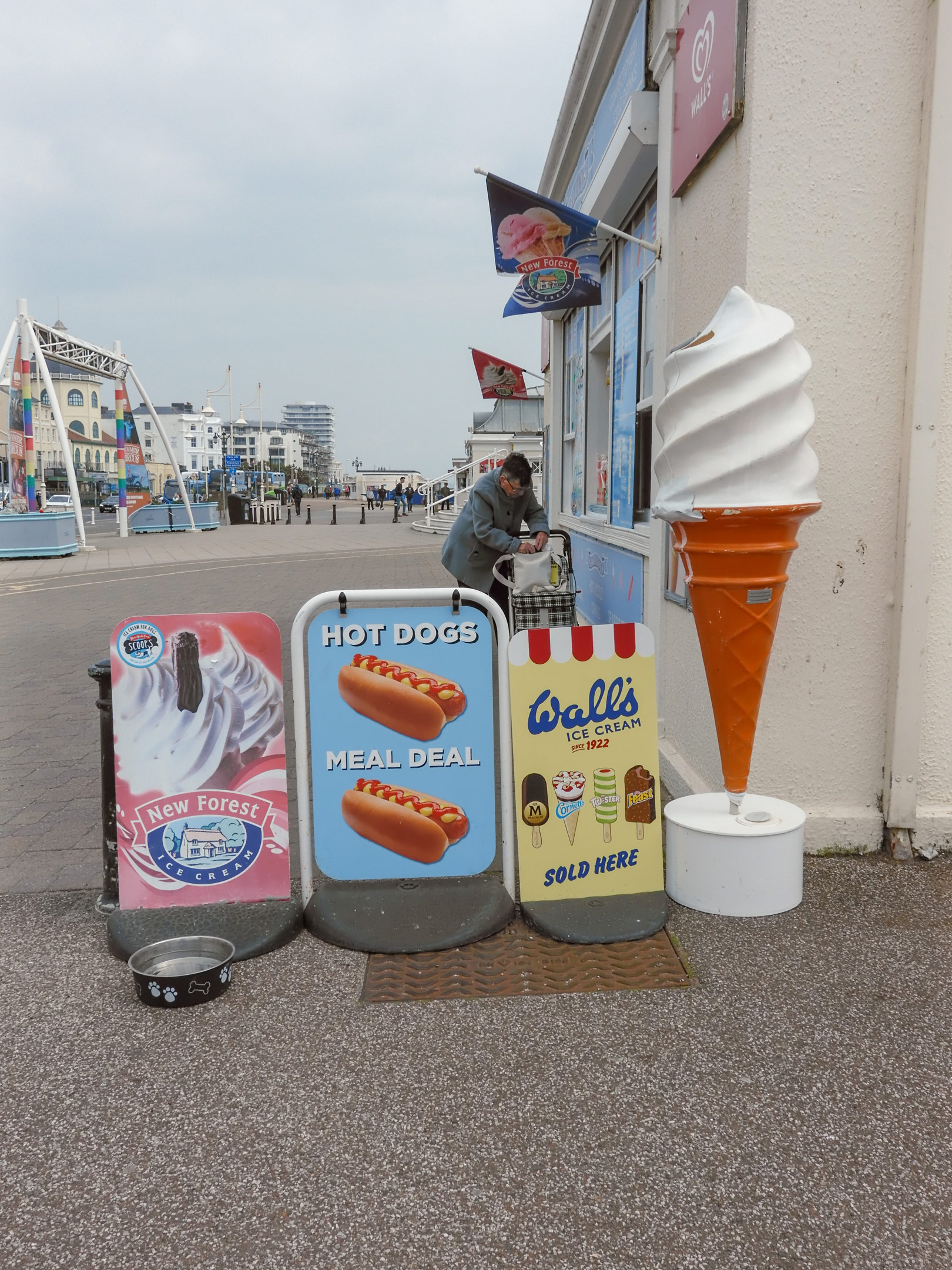 Ein Geschäft mit Werbeschildern für Eiscreme und Hot Dogs an der Strandpromenade von Worthing. Im Hintergrund wird eine Person bedient.