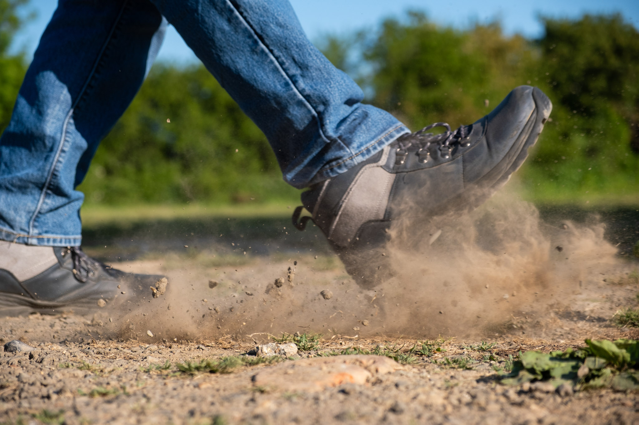 A person kicking the ground pushing lots of dust into the air