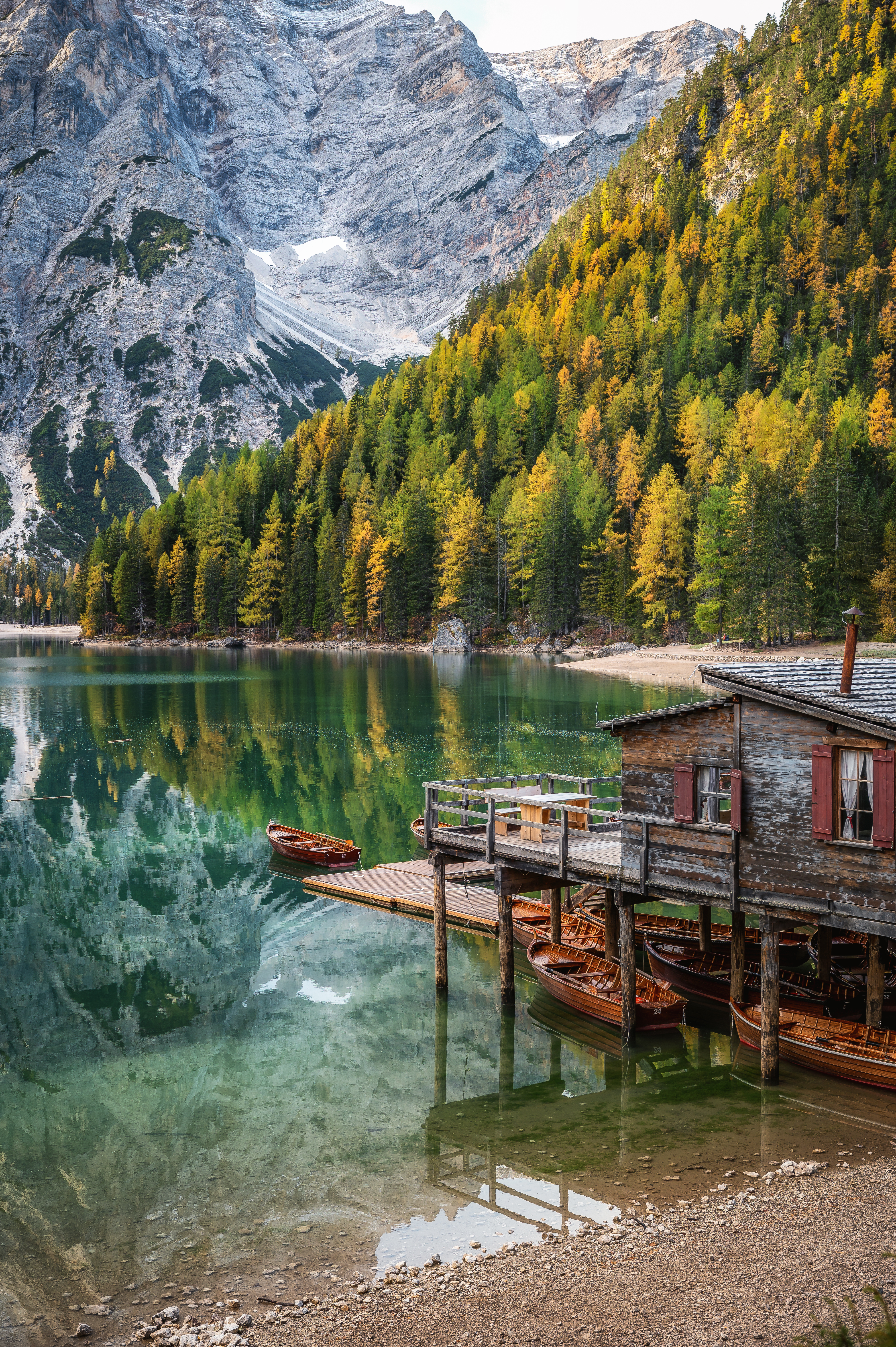 Vista sul Lago di Braies con acqua verde smeraldo, barche di legno, un molo con baita e montagne innevate sullo sfondo.