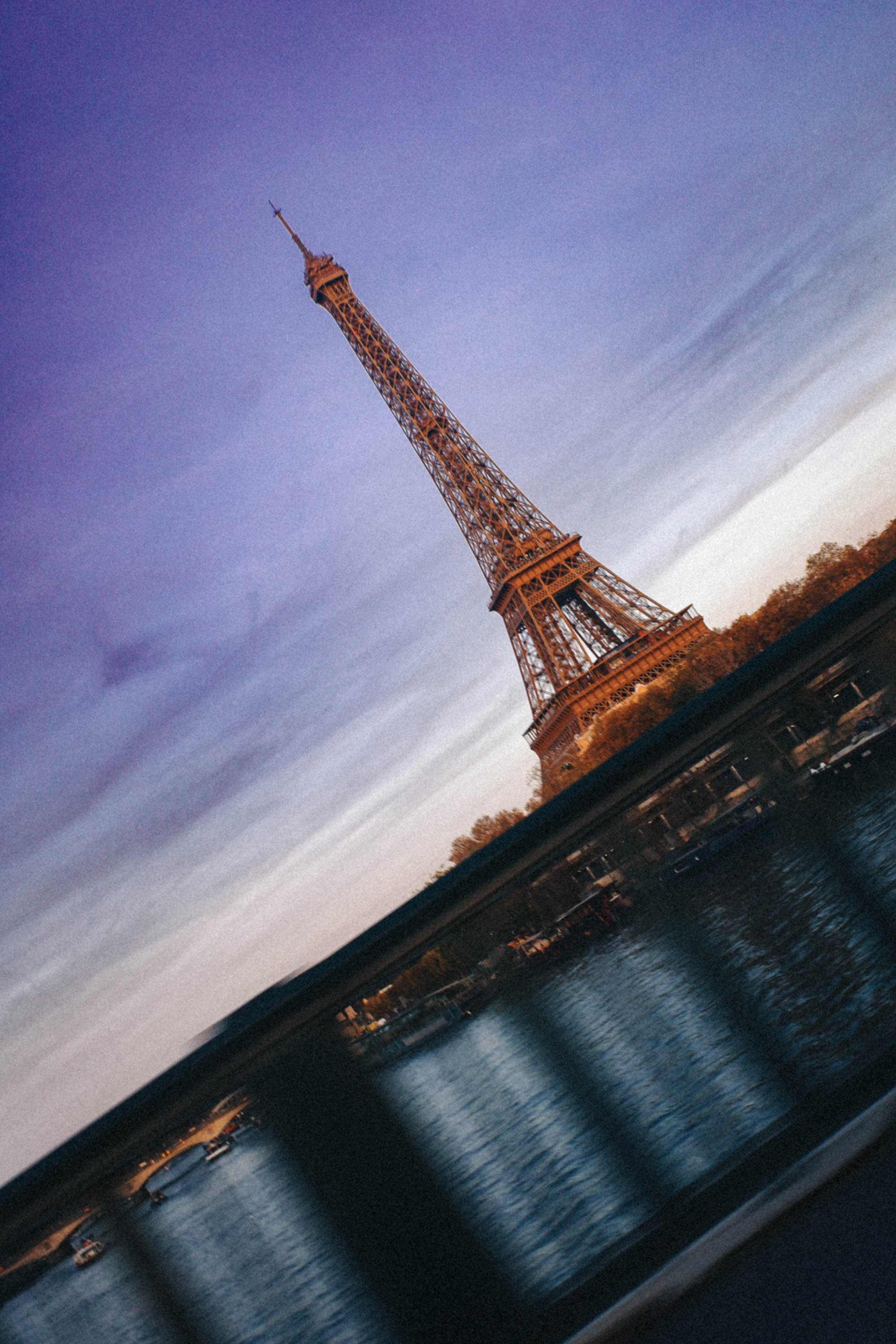A golden-hour look at the Eiffel Tower from the Seine, photographed through the bridge railing for a unique, atmospheric angle. Shot by Wesley Verhoeve on a Fujifilm XF10.