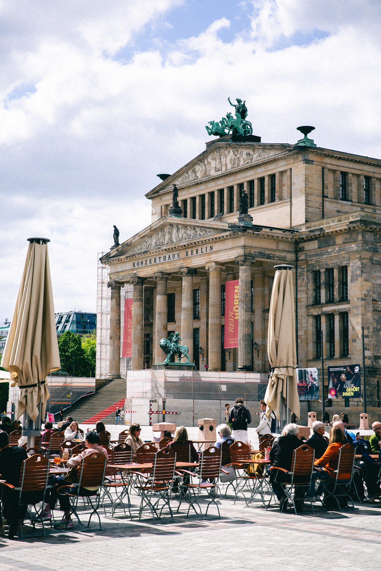 Photograph of the Konzerthaus at Berlin’s Gendarmenmarkt, with people seated at outdoor cafe tables beneath a bright, cloudy sky. Shot by Austin Fassino on a Canon EOS 5D Mark III.