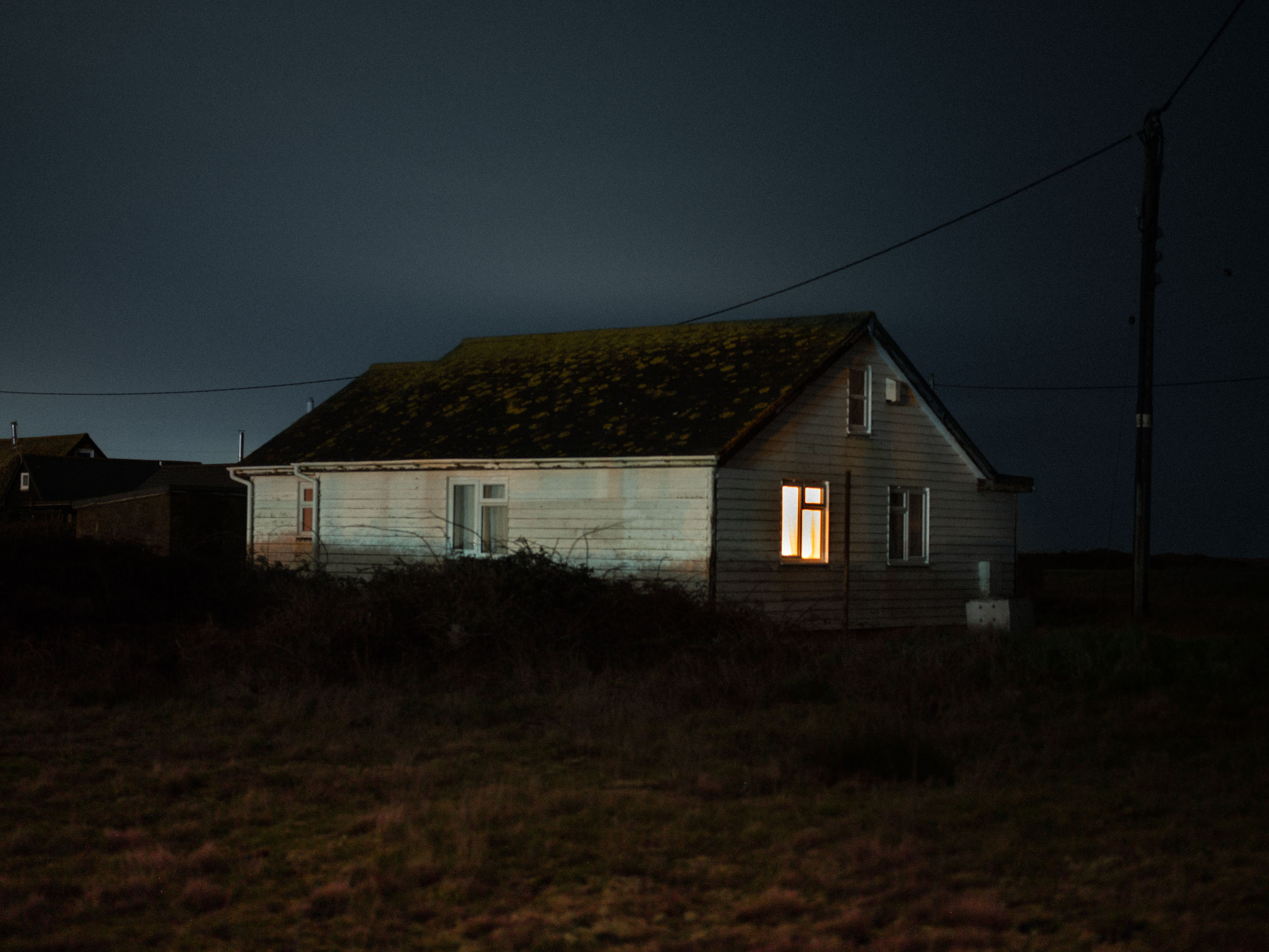 A night-time shot of a house with a single light on, shot on Phase One P45 Plus by Ian Howorth