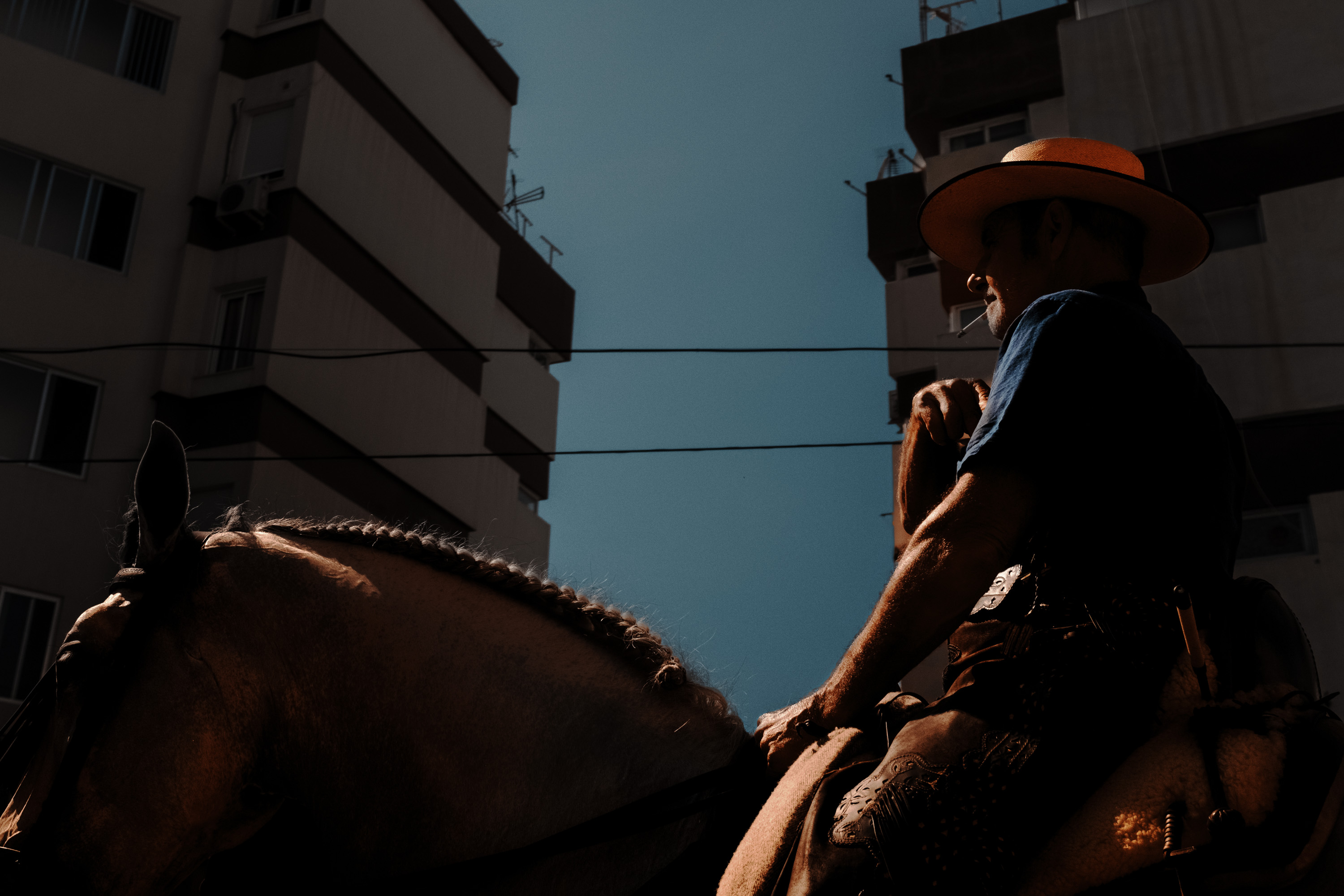 A person cast in shadow riding a horse with a wide-brimmed hat. By Ian Howorth.