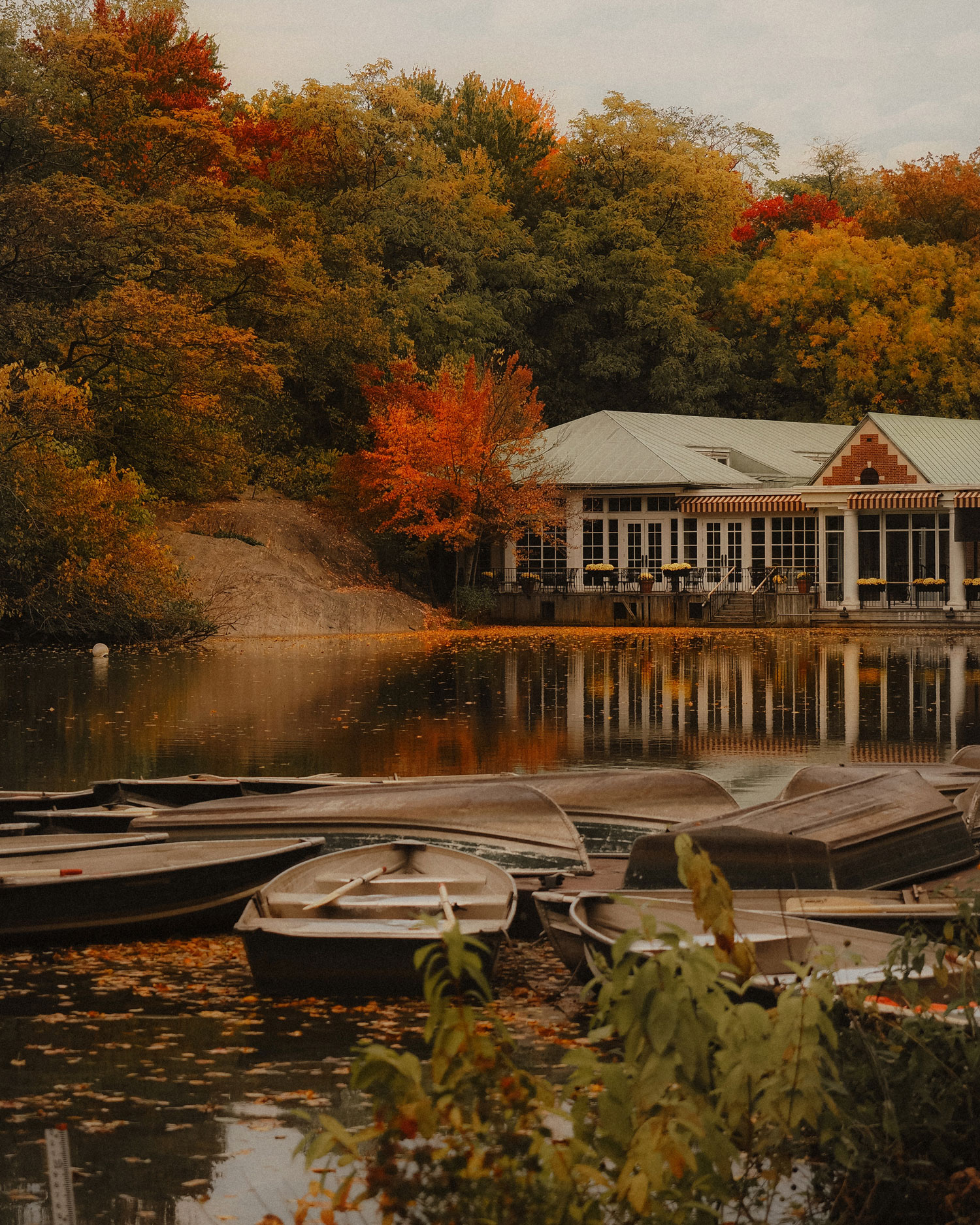 A building on the side of a lake in Central Park. There are small boats in the foreground and trees in the background. Shot on an Olympus E-M5 III by Georgina Lamrock