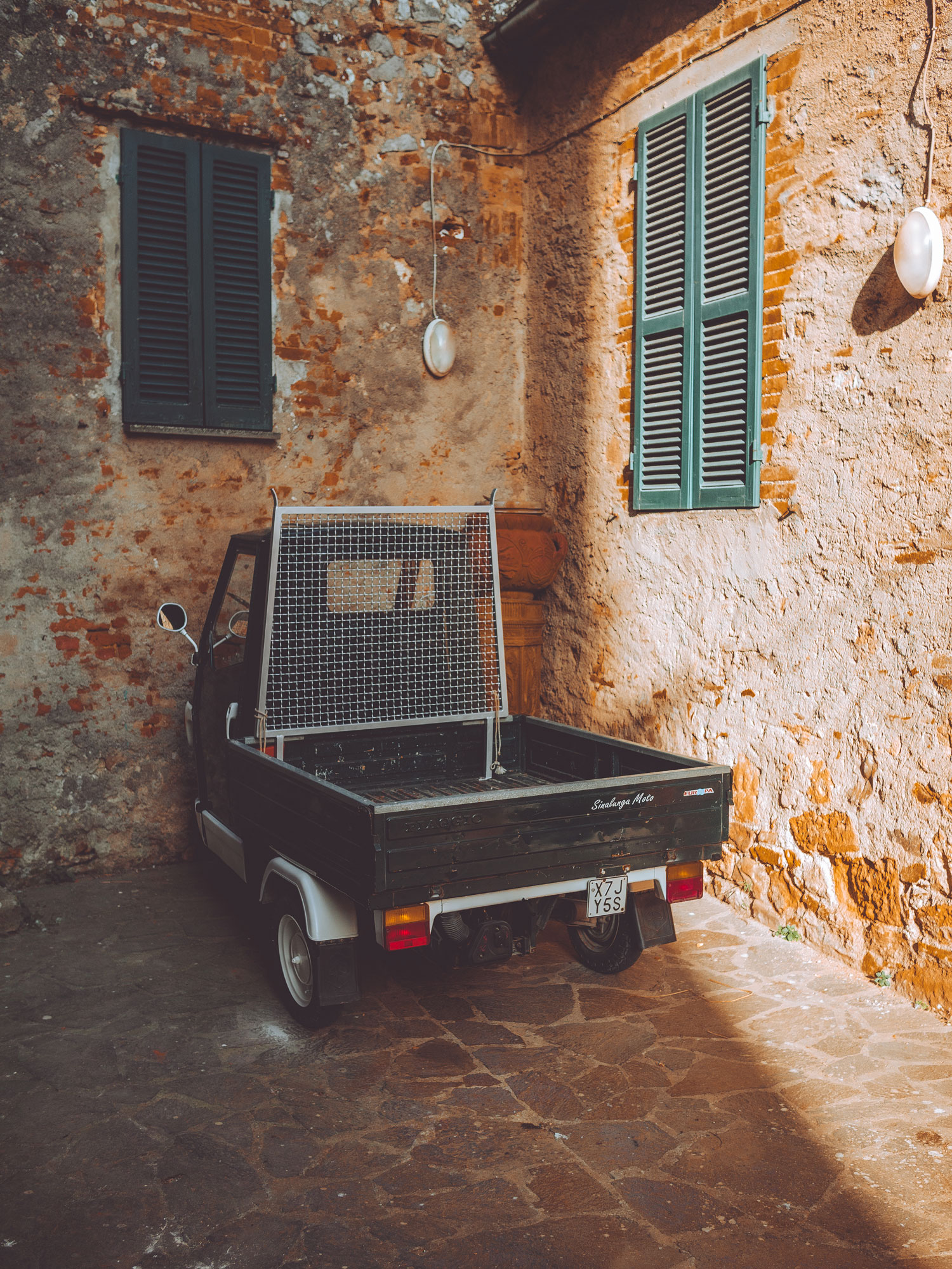 A small black pick-up van parked next to two walls, there are closed shutters on each wall.