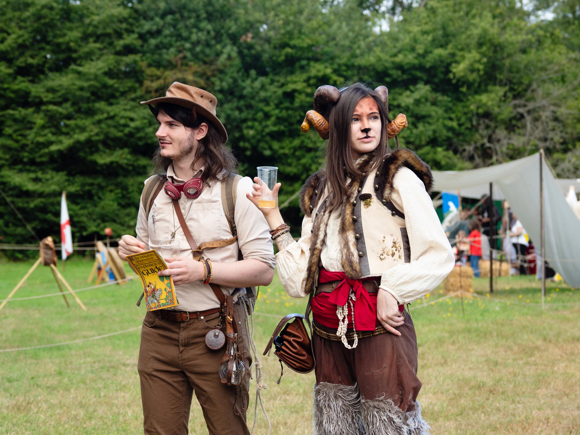 Two people dressed in costume at a medieval festival. One is wearing horns and is dressed in faux animal fur; the other is holding a guide.