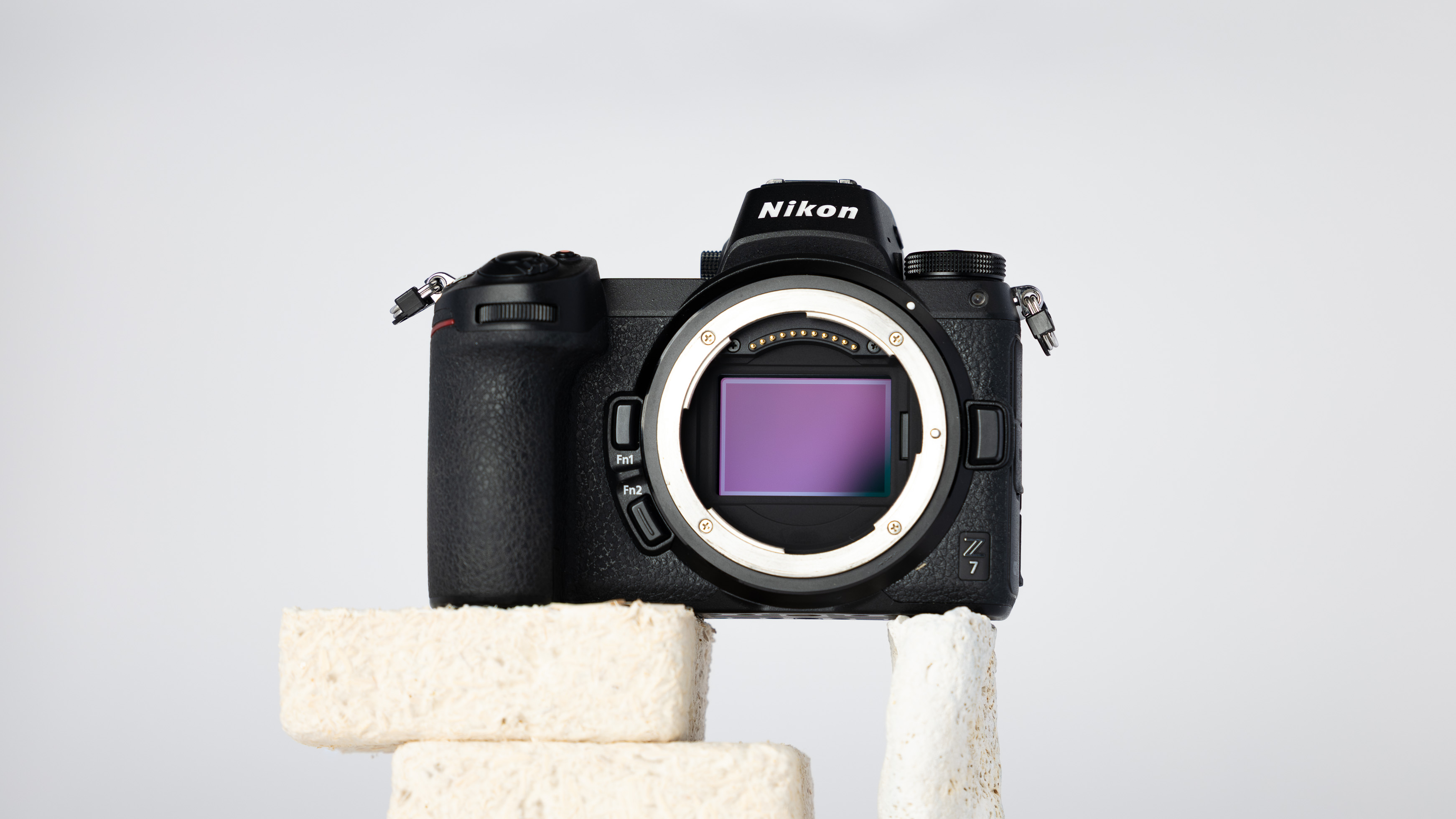 A product shot of a secondhand Nikon Z7 camera propped up on a rocky podium on an off white background.