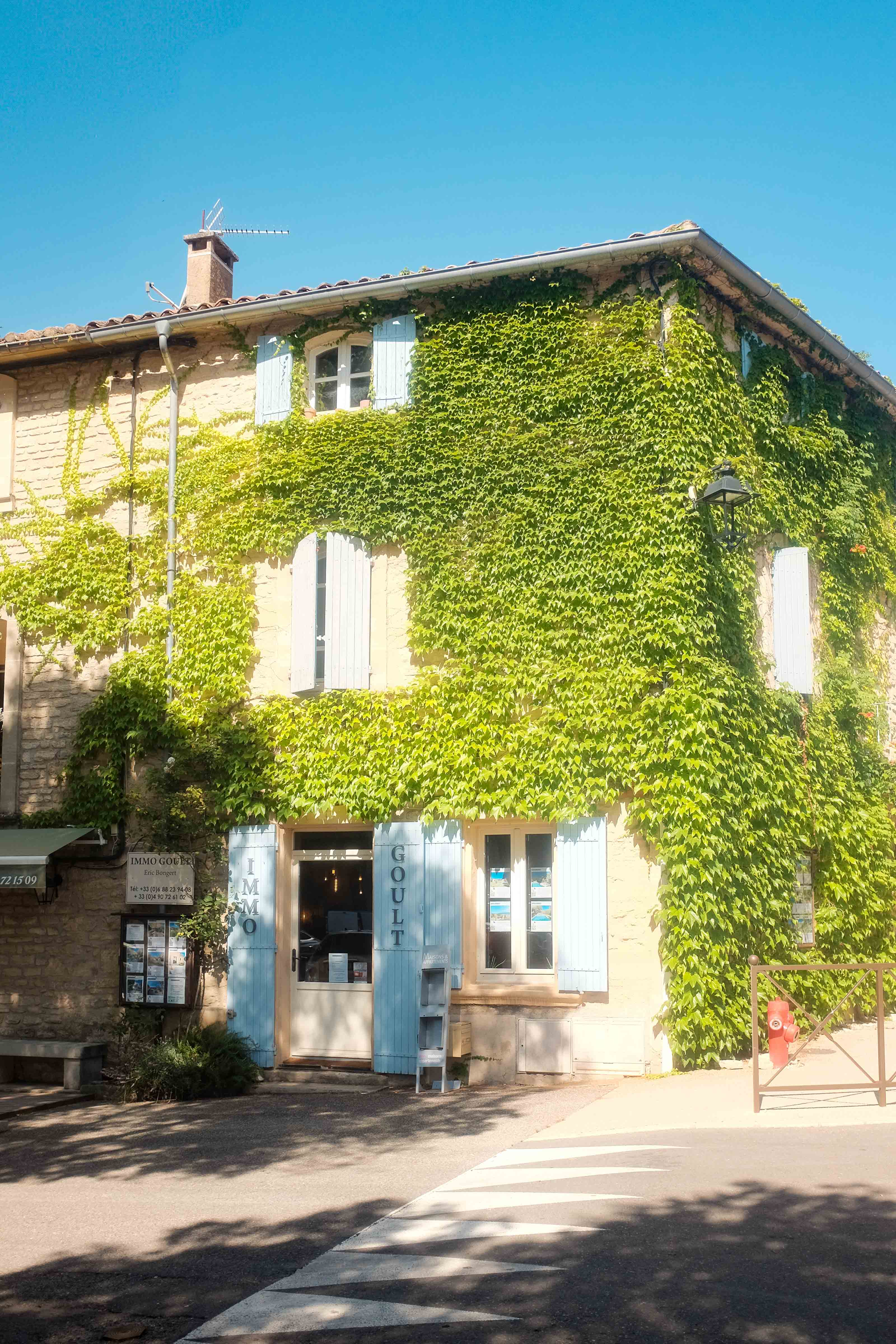The corner of a street in Gordes, France that has green leaves all over the building. Taken on the Fujifilm X100T by Connor Redmond.