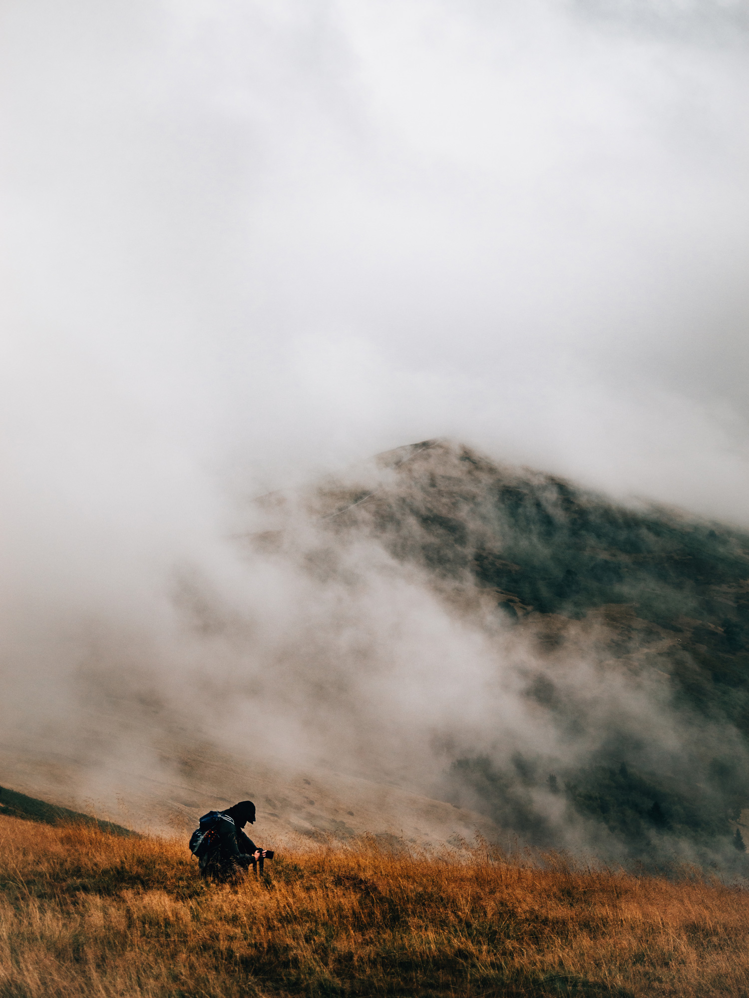 A person crouching on a hilltop, with clouds in the background, shot by Emily Lowrey with the Panasonic Lumix DC-GH6.