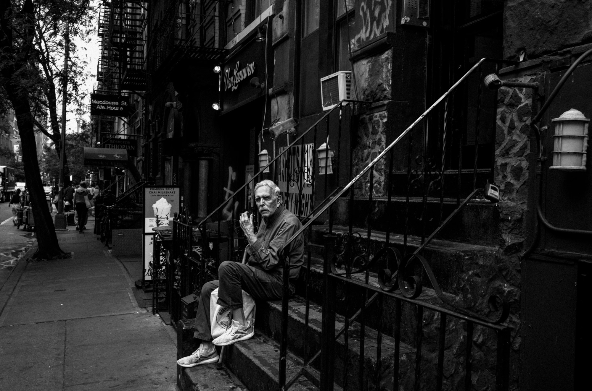 A black-and-white photo of an elderly person sitting on a stoop