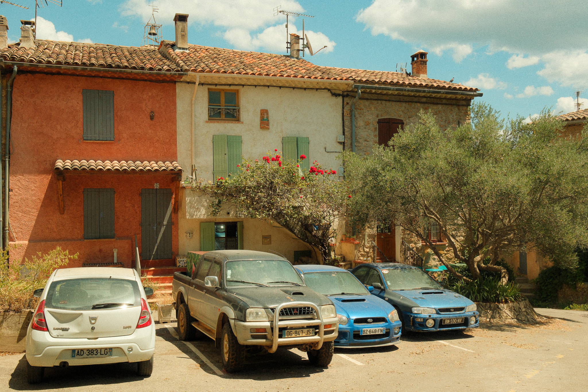 A bright midday sunny scene showing cars parked covered in dust, in a sleepy village in Provence, France. 
