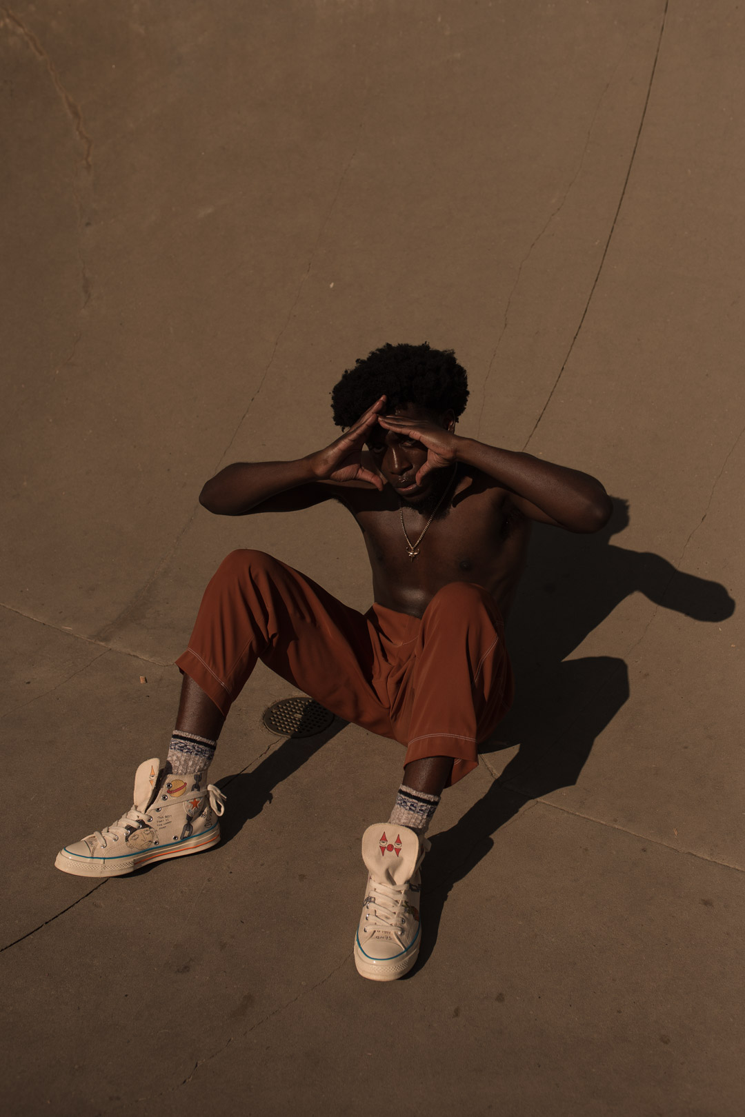 Photo d'une personne noire assise sur du béton au soleil, les mains devant le visage.