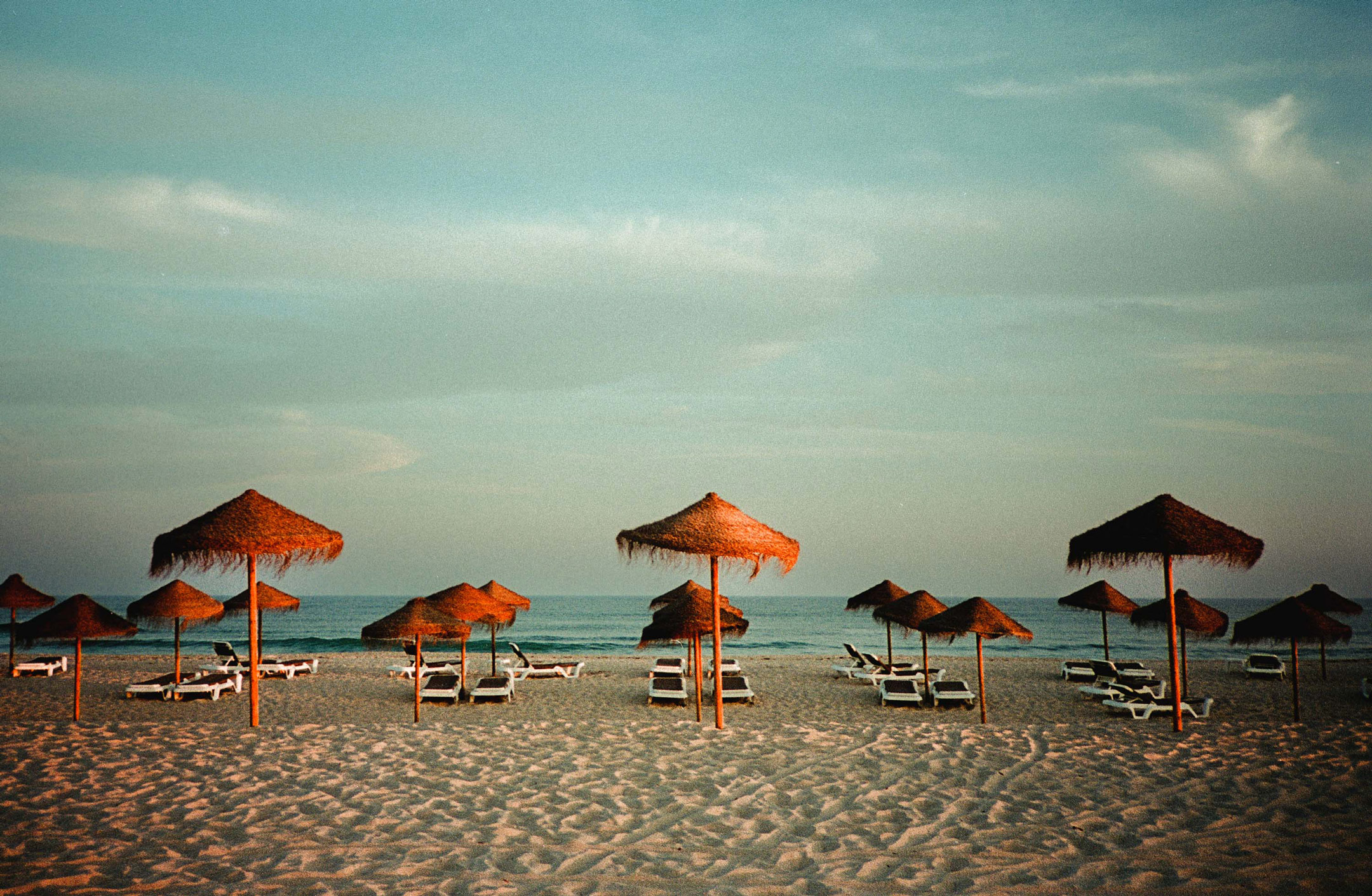 A beach with many sunbeds and straw parasols by Ian Howorth