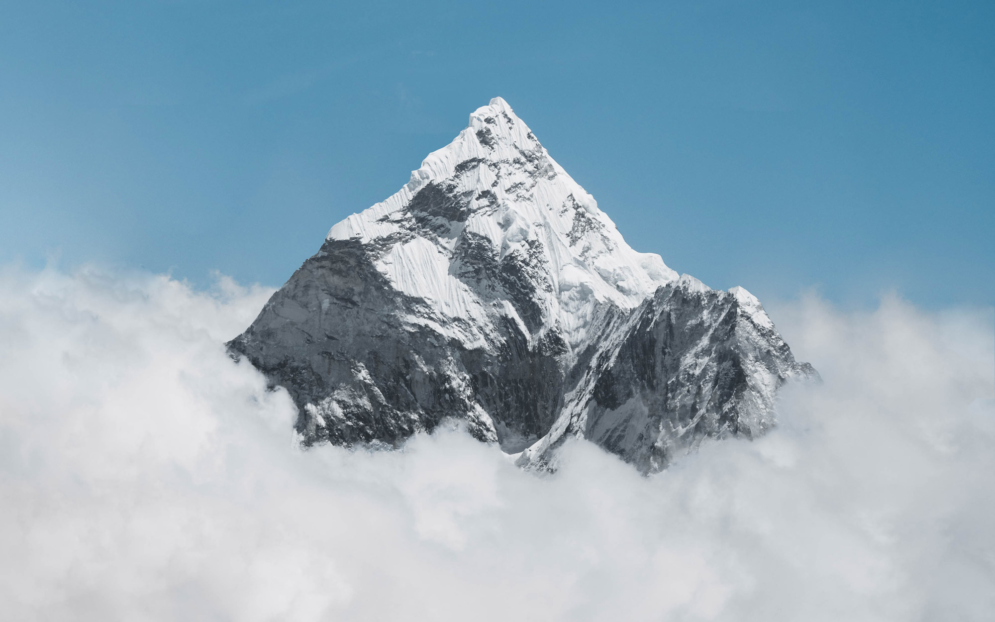 A snowy mountain peak pierces the clouds, with a blue sky in the background, shot by Jack Anstey with the Sony Alpha A7 IV and the Sony FE 70-200mm f/4 G OSS.