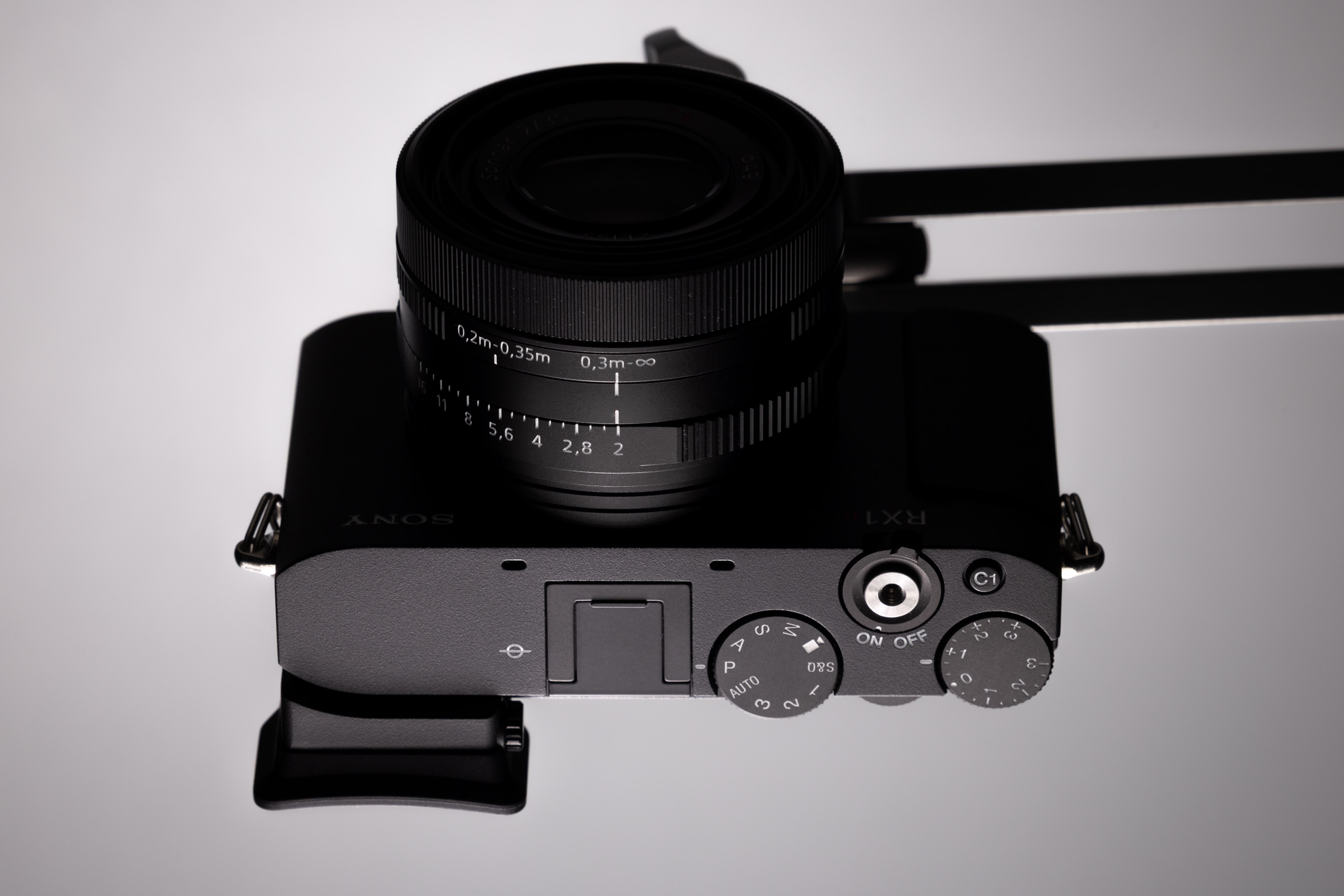 Draufsicht auf die Sony RX1R III mit dem fest verbauten 35-mm-Objektiv von Zeiss, Blenden- und Fokusringen, Auslöser und Belichtungsrädern vor einem Studiohintergrund.