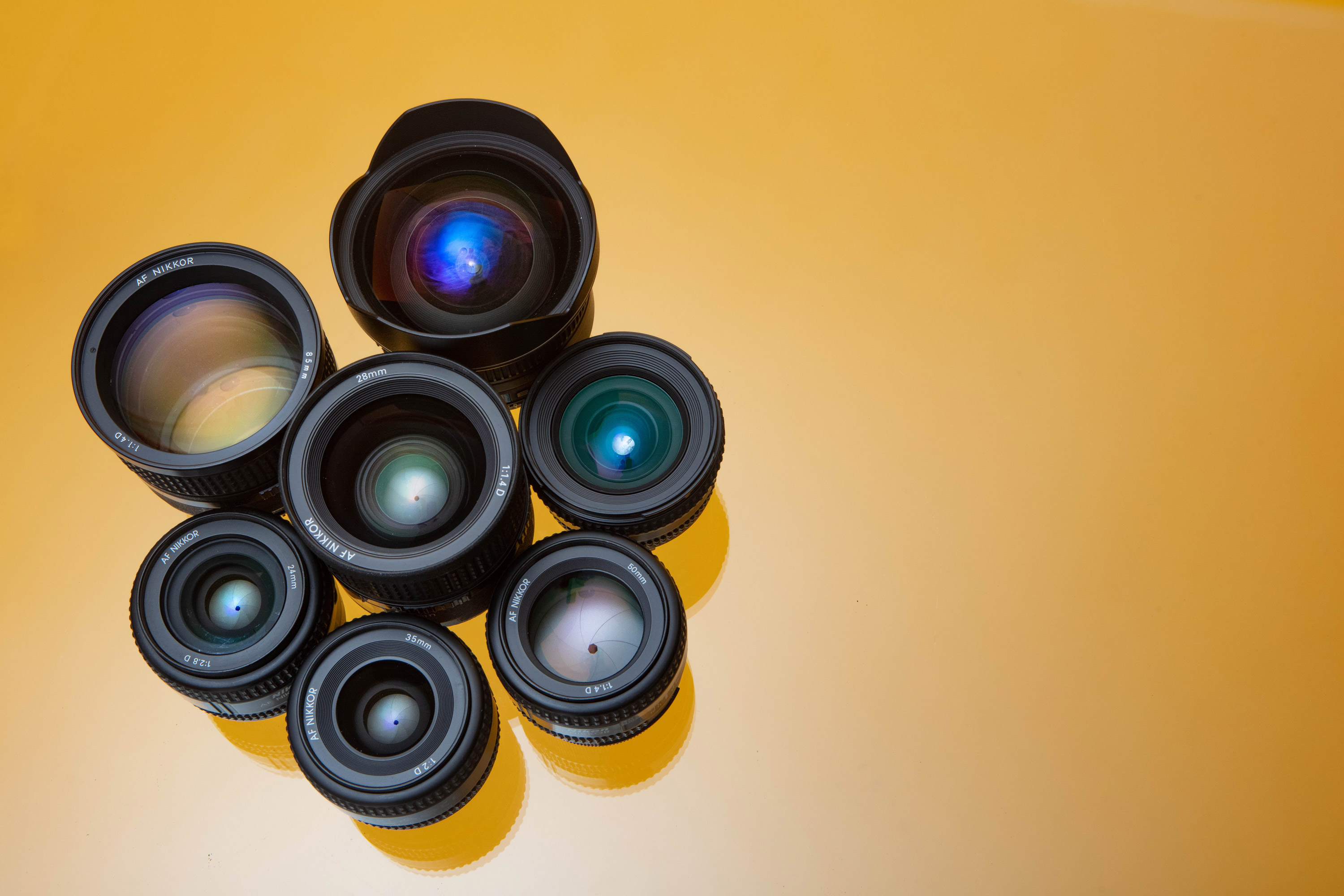 Uma disposição de sete lentes Nikon organizadas em círculo sobre um fundo amarelo