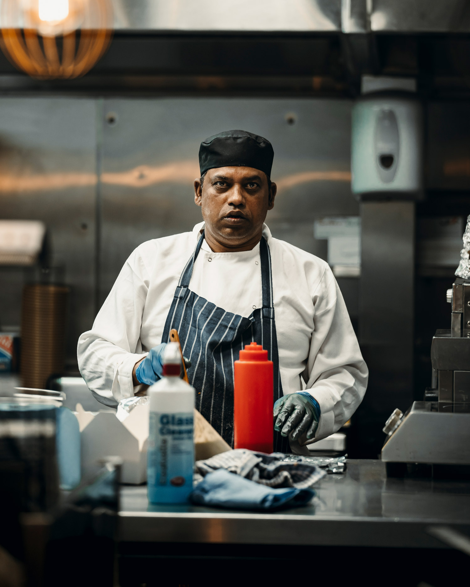 A chef wearing an apron stands in front of various sauce bottles in a kitchen