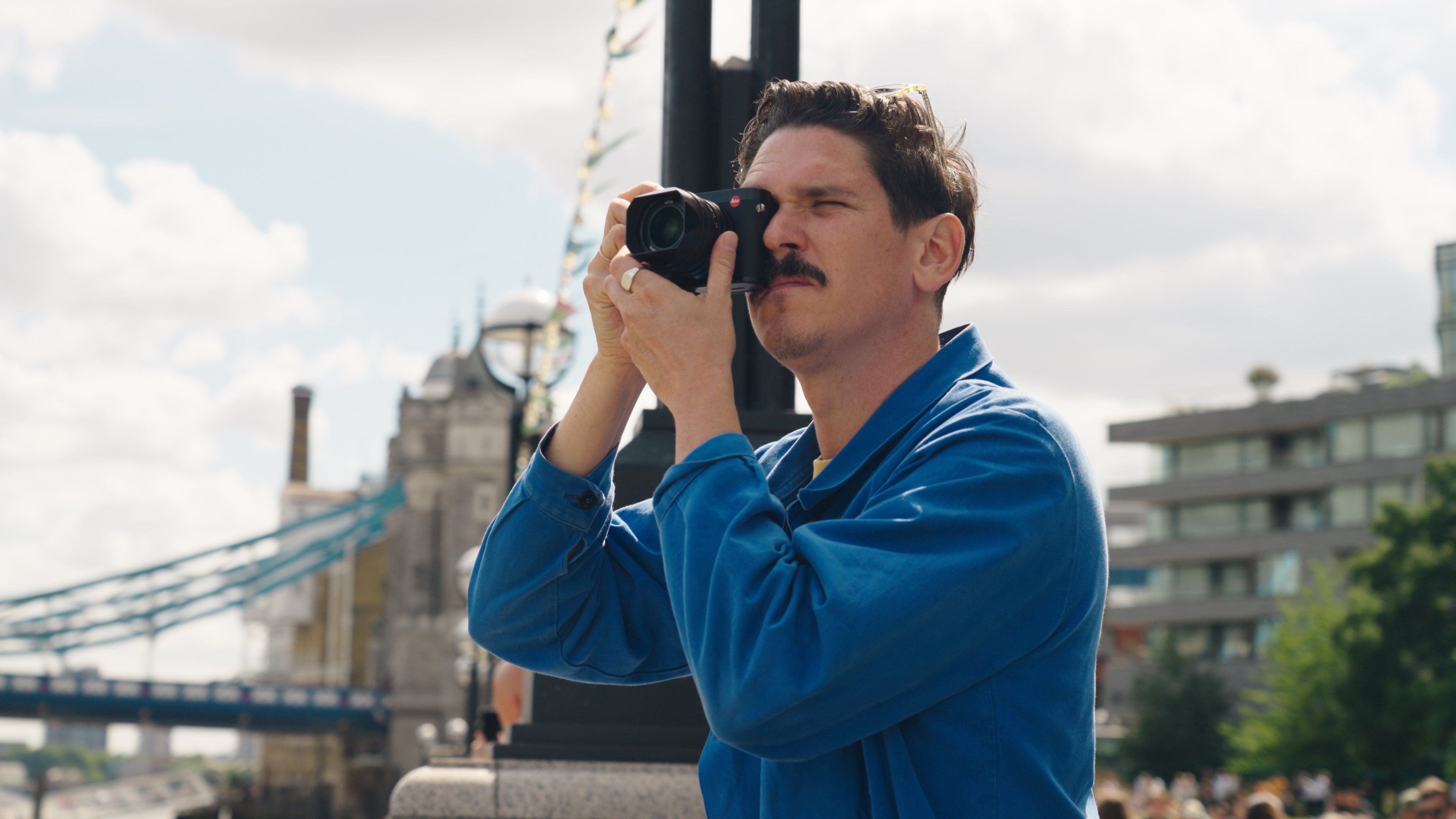Ein Foto des Fotografen Ian Howorth, ein blaues Hemd tragend, der die Tower Bridge in London mit der Leica Q2 fotografiert.