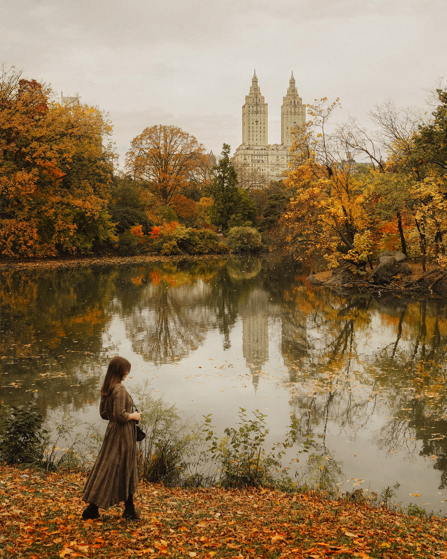 Georgina Lamrock stands by a lake in Central Park, with buildings and trees in the background. Shot on an Olympus PEN F by Georgina Lamrock.