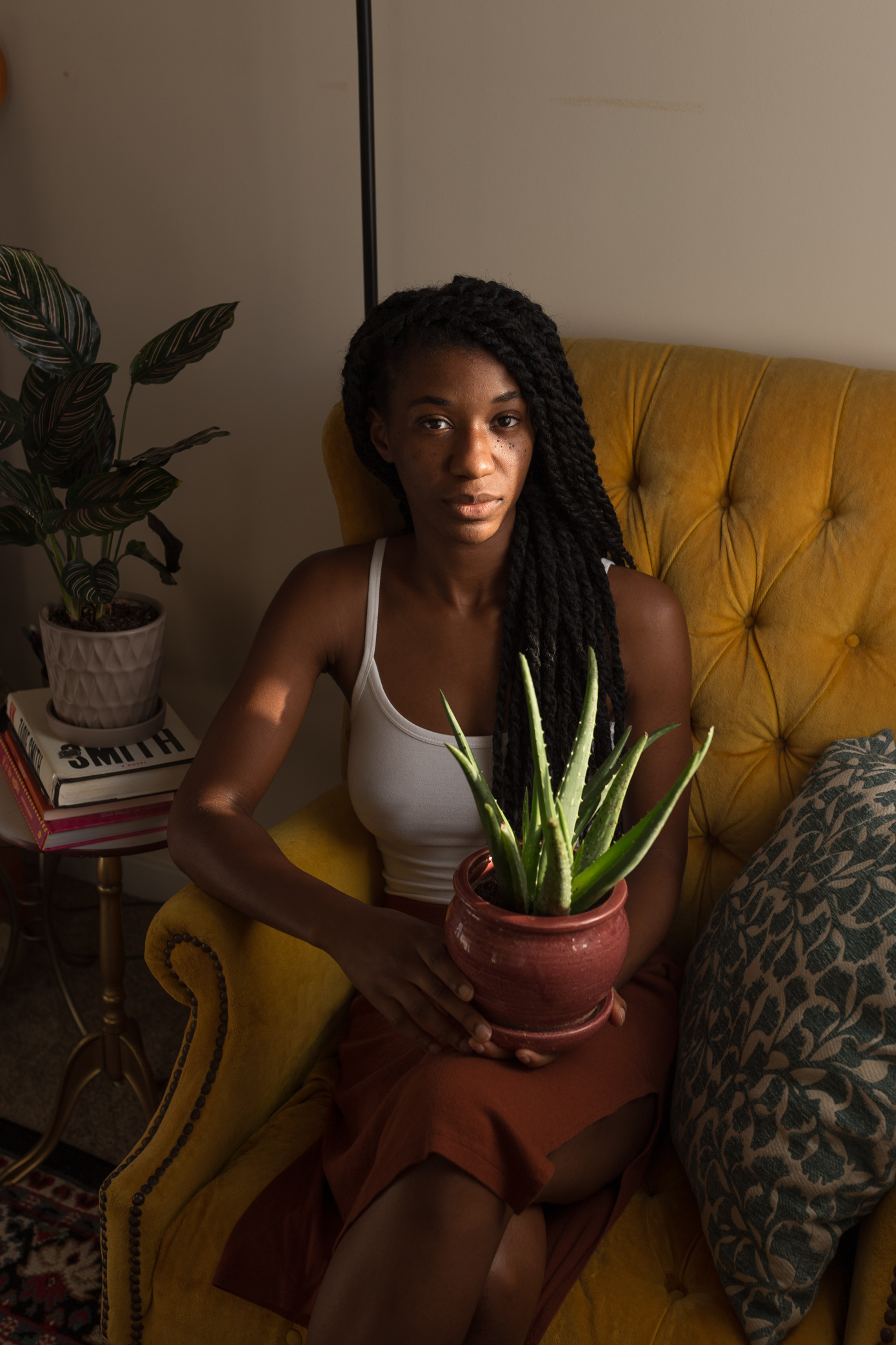 Photo of black woman sitting on a yellow chair holding a succulent plant in an orange pot.