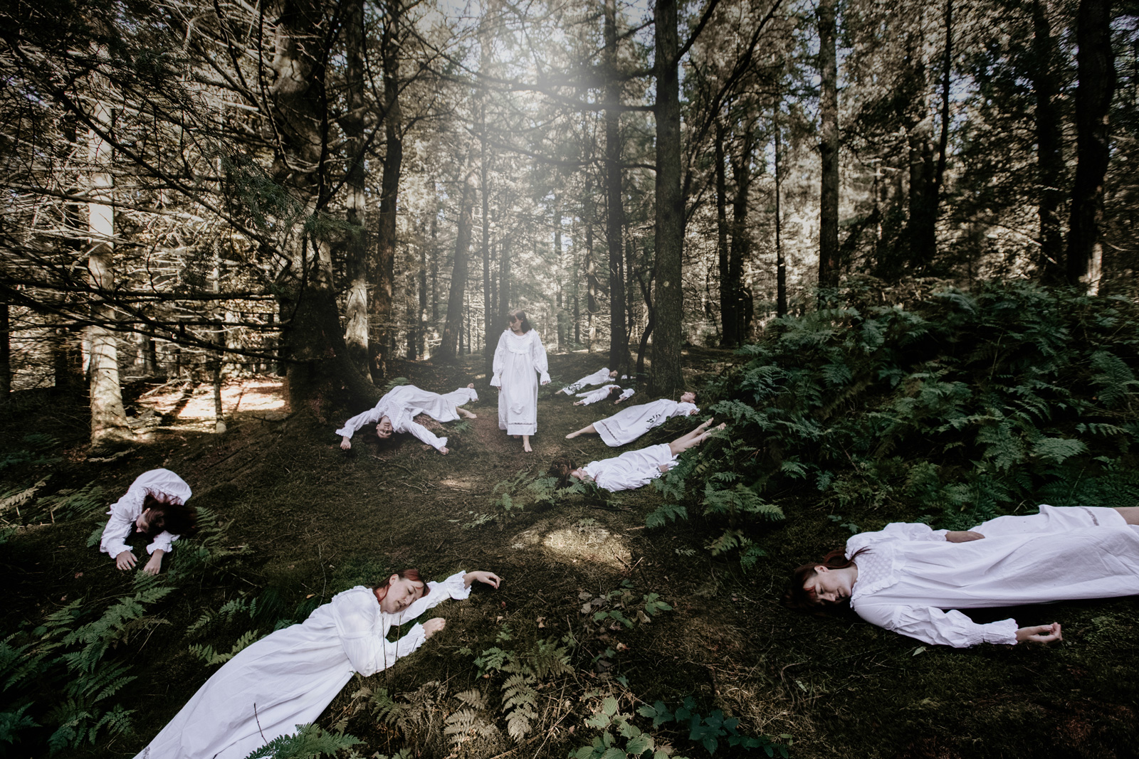Kleurencompositie horrorfoto van een model in een witte jurk dat langs meerdere versies van het model op de grond loopt