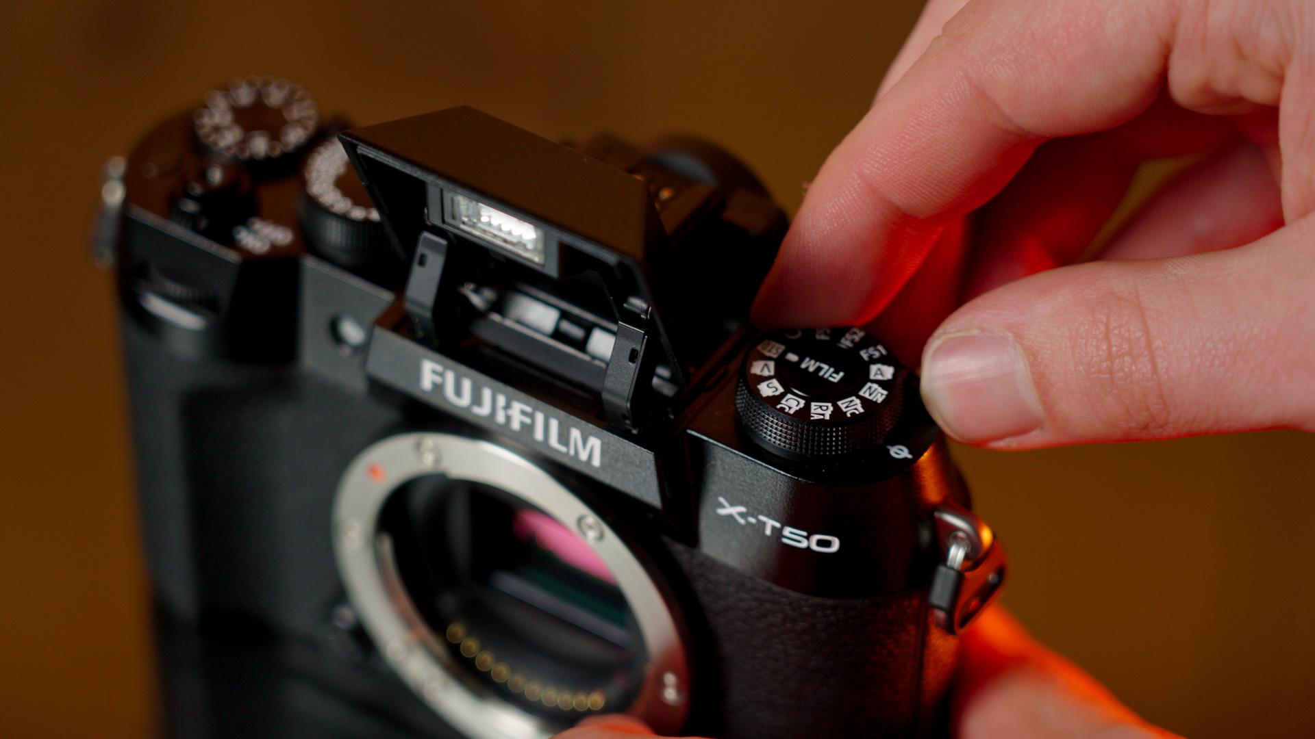 
Un gros plan du Fujifilm X-T50, avec son flash exposé, alors qu'une paire de mains ajuste le cadran de simulation de film.

