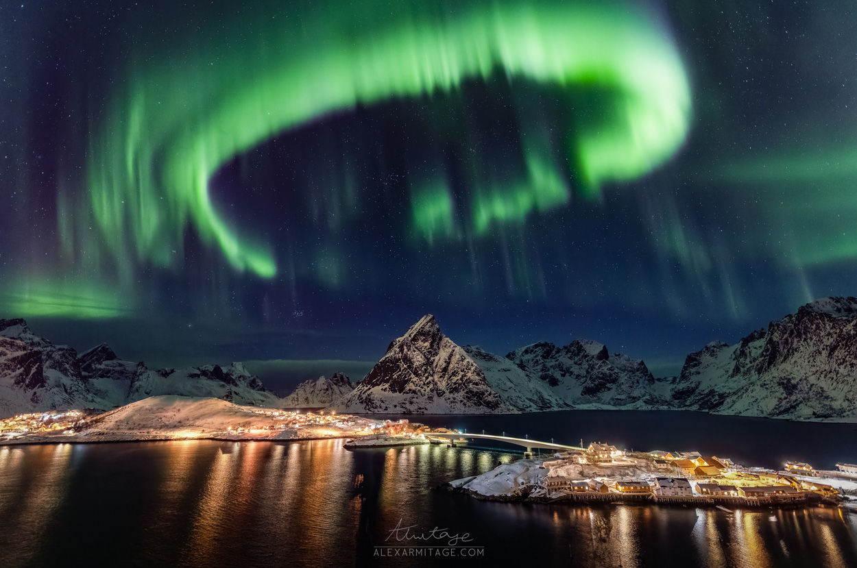 Green lights fill the sky above a mountain at night.