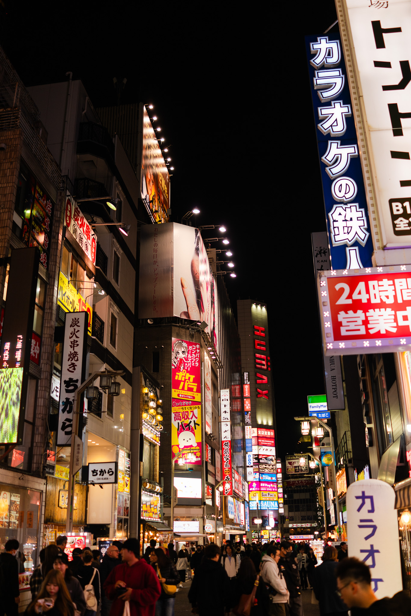 Tokyo's nightlife, a crowded street illuminated by vibrant neon signs and billboards, capturing the essence of urban Japan. Photographed by Ruby Cruden with a Sony DSC-RX1 RM II.