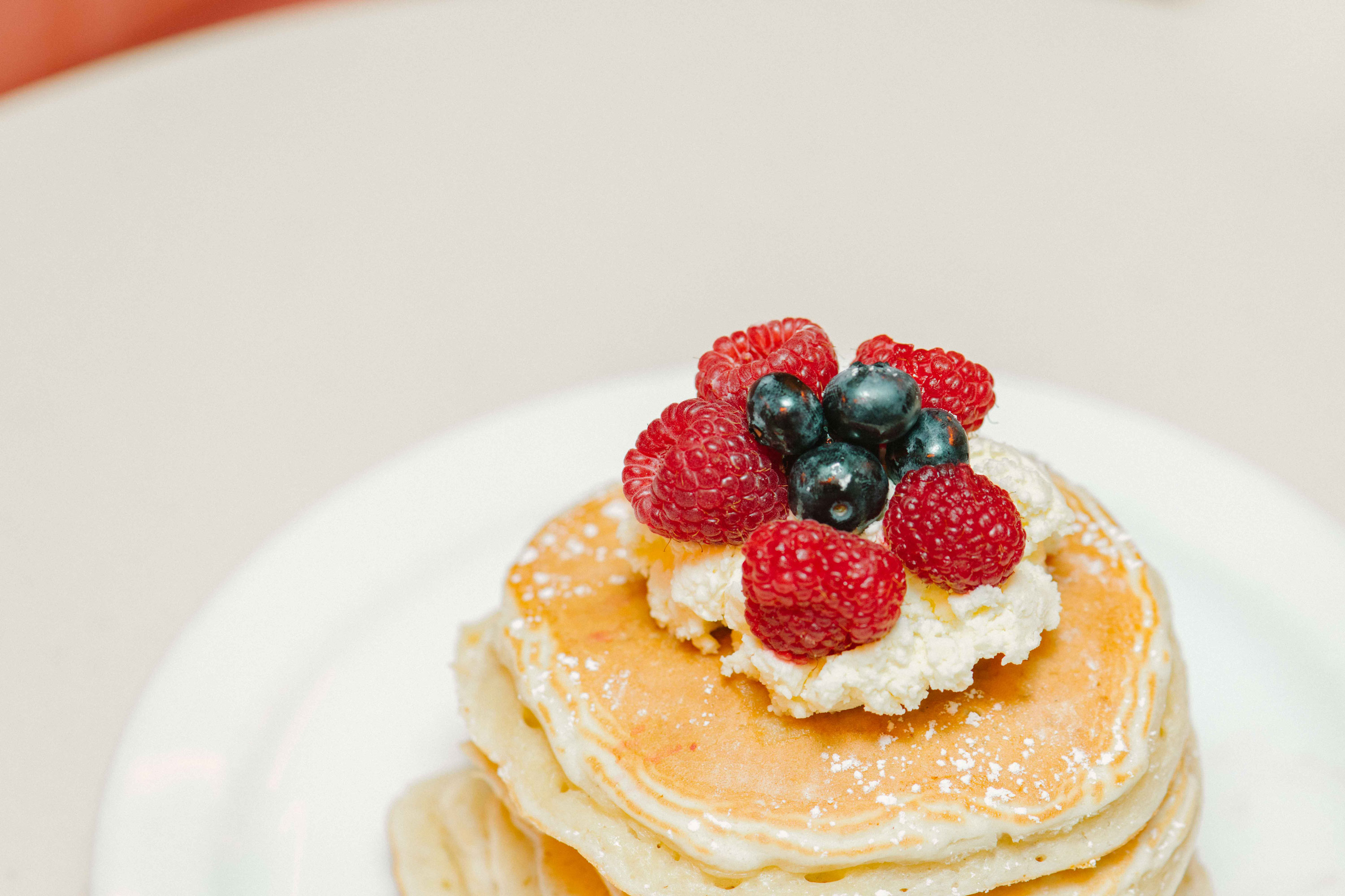 Nahaufnahme eines Stapels Pancakes mit Schlagsahne, Himbeeren und Blaubeeren