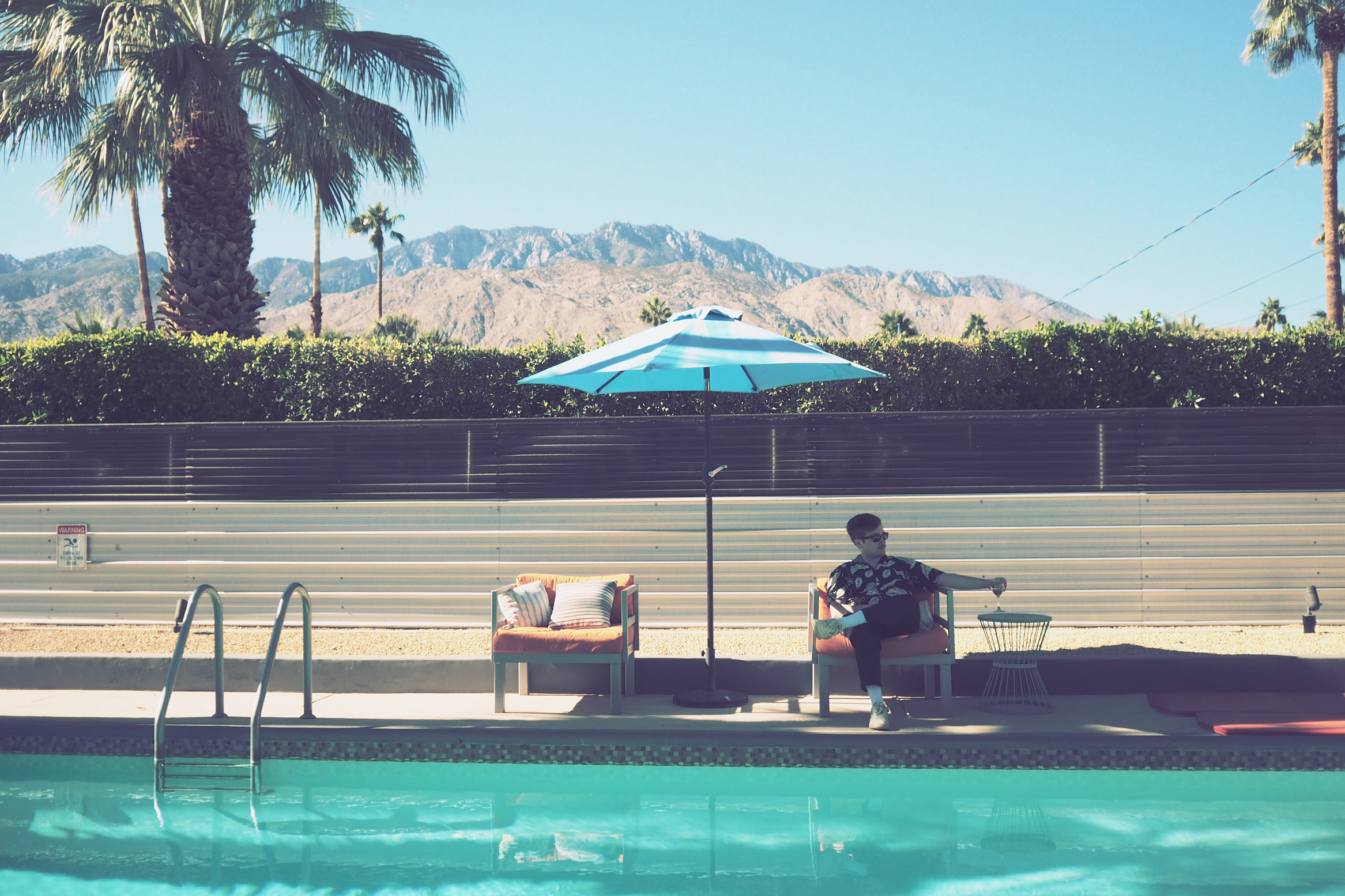 Man sitting poolside under an umbrella in Palm Springs, California, taken on an Olympus Pen-F by Justin Patricolo.