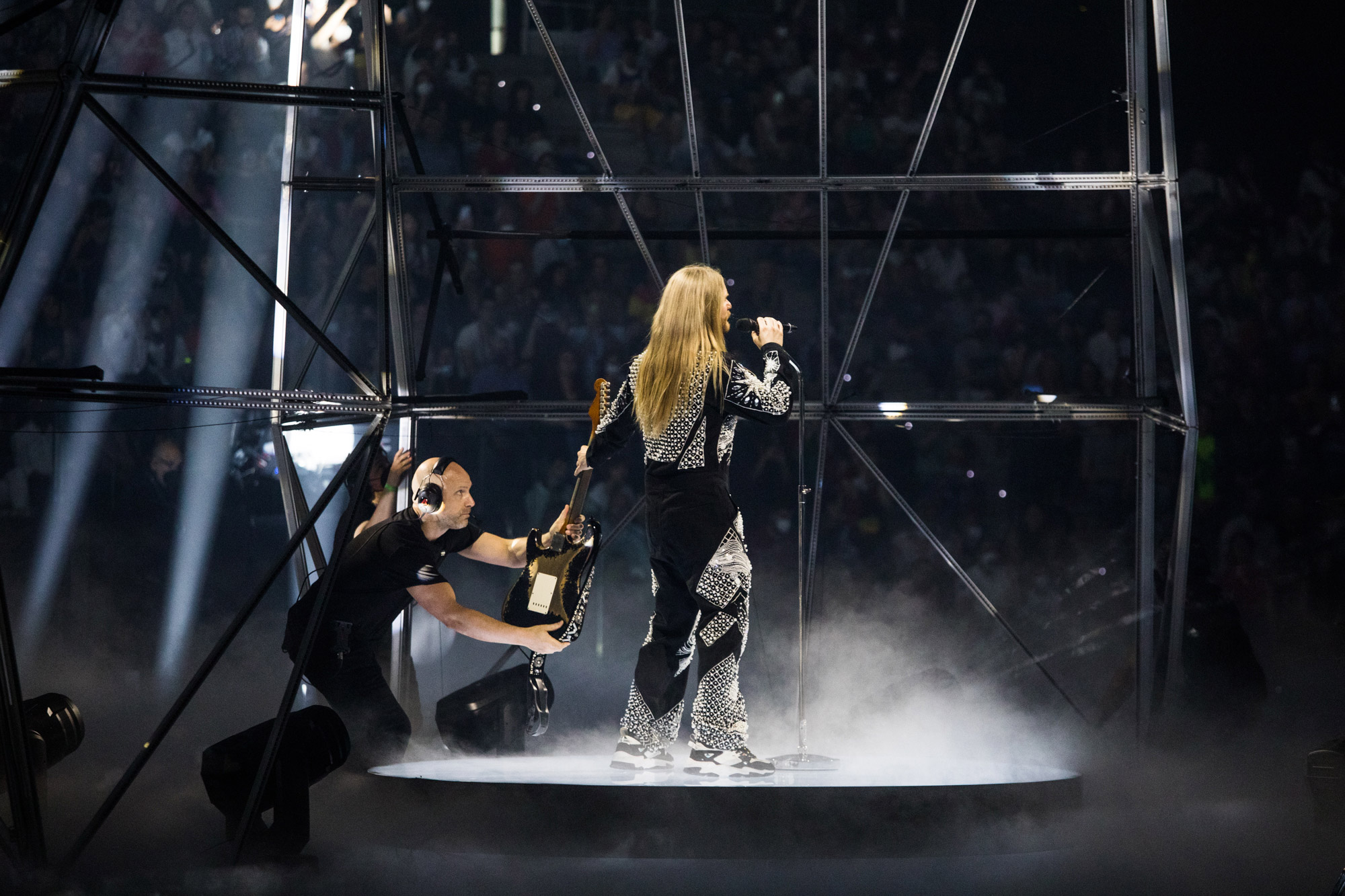 A person hands Sam Ryder his guitar on stage at Eurovision.