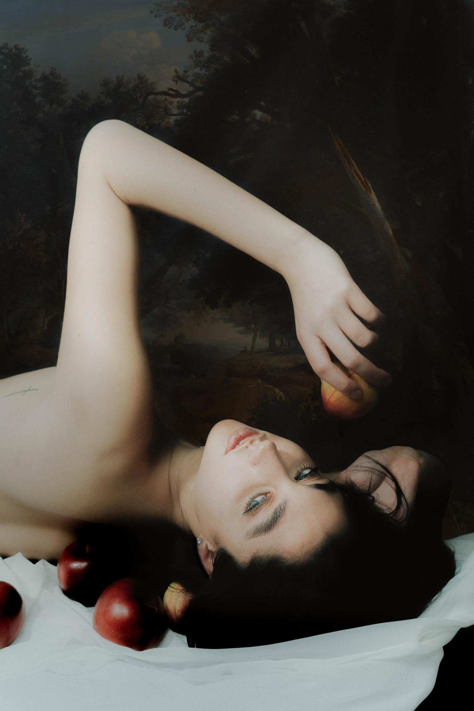 A model with bare shoulders lies upside down on a sheet surrounded by apples, with one apple in their hand, shot by Isabel Malia with a Sony A7 III