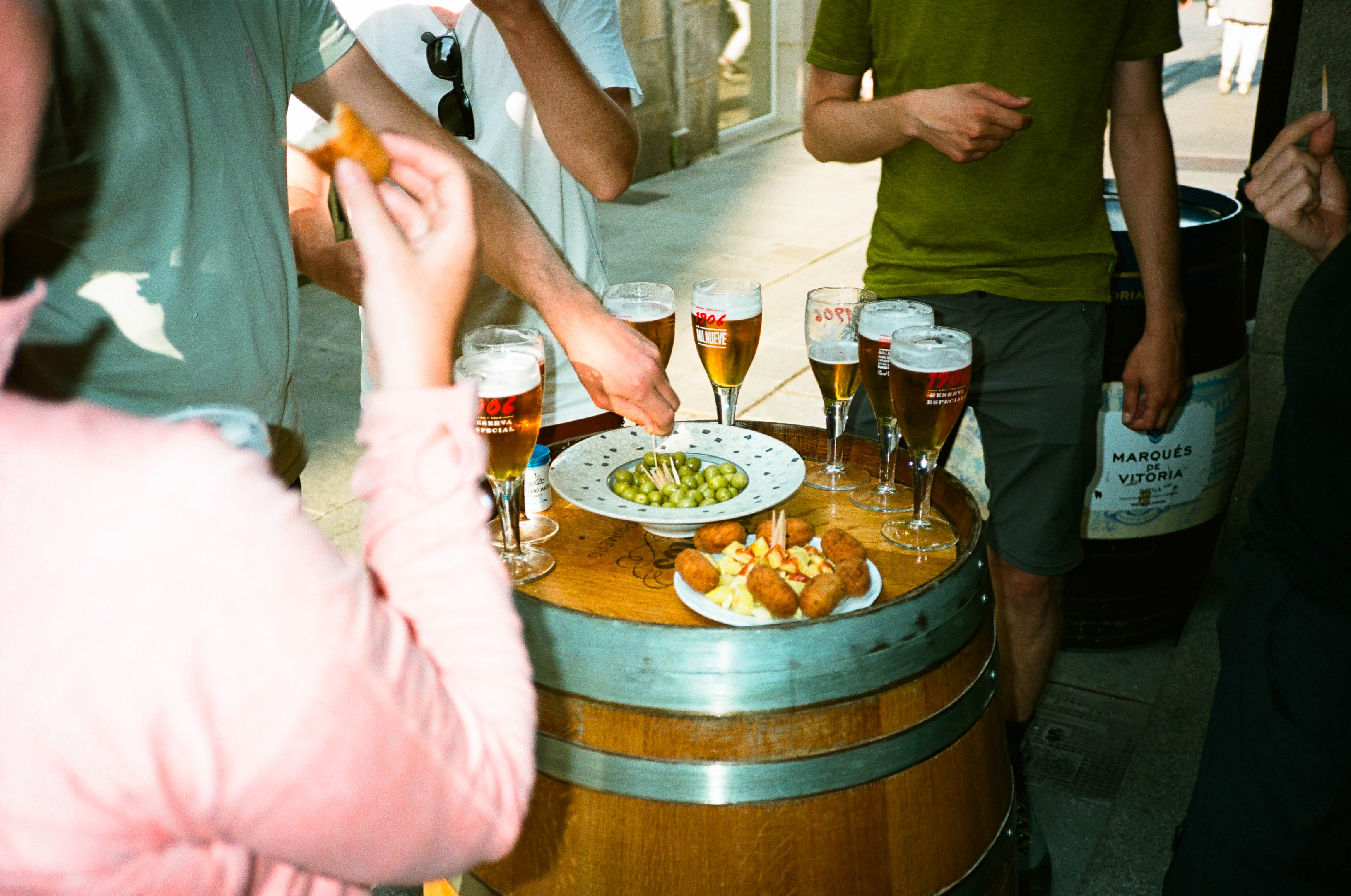A group of pilgrims on the Camino Primitivo trail stop for a lunch snack with beer in Lugo. Olives are being skewered. By Connor Redmond.