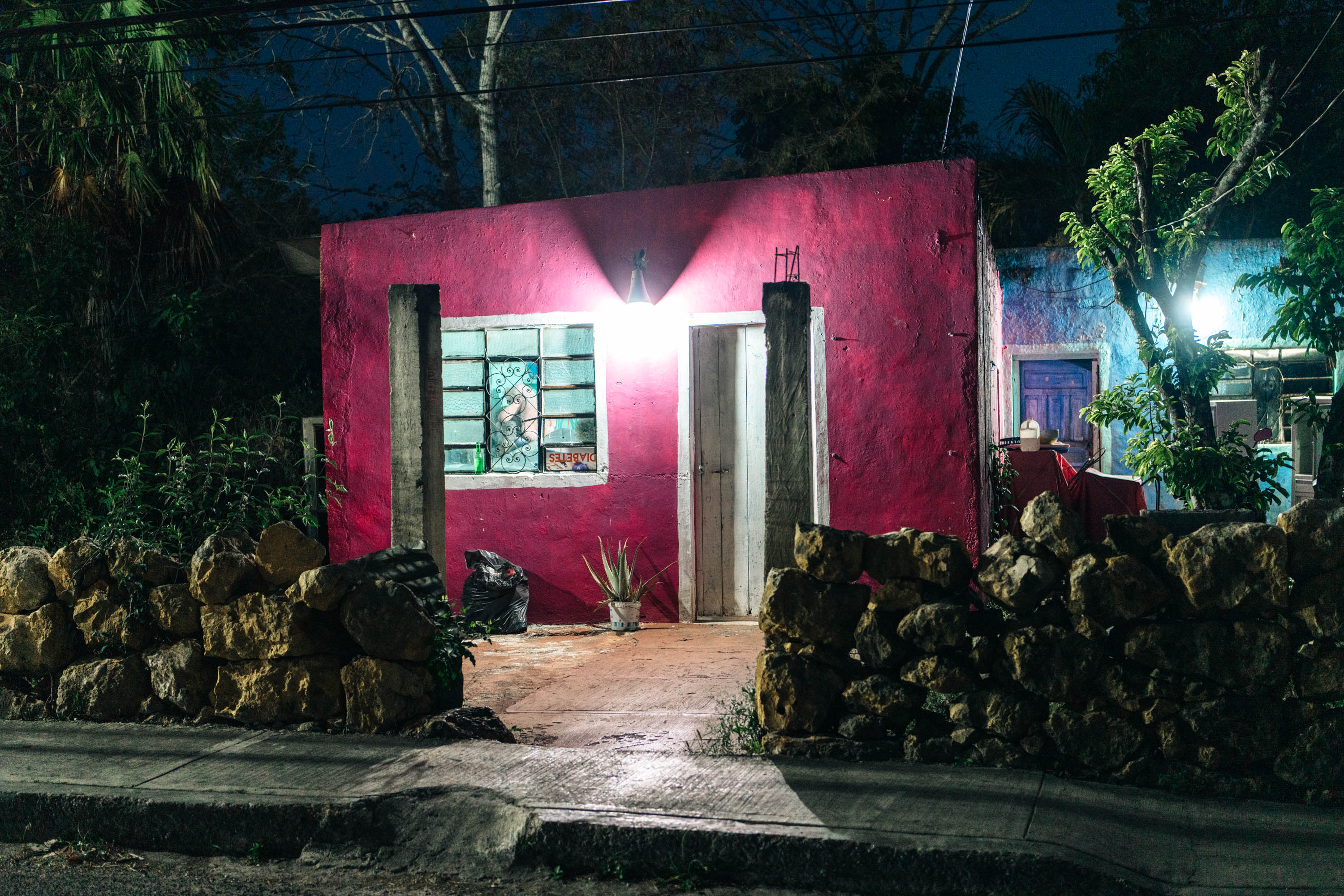 Een helder, levendig roze huis in Mexico wordt 's nachts verlicht door straat- en huisverlichting. Gefotografeerd door Ian Howorth.