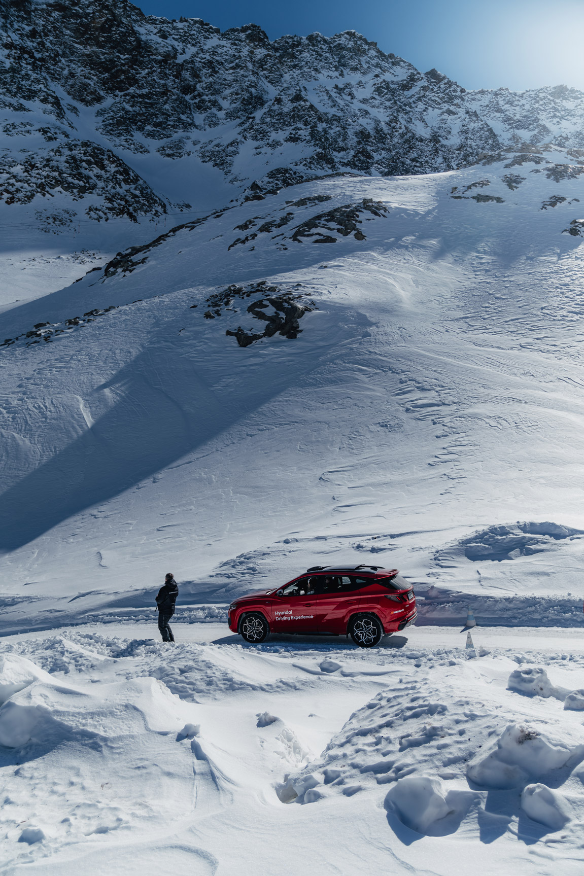 Red car and man stand on snowy mountaintop in Austria