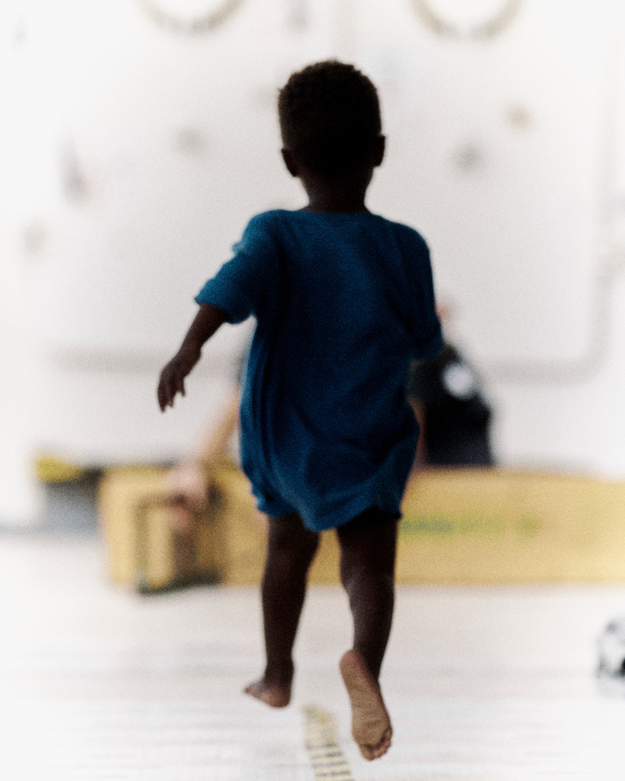 Child photographed from behind running barefoot away from the camera.