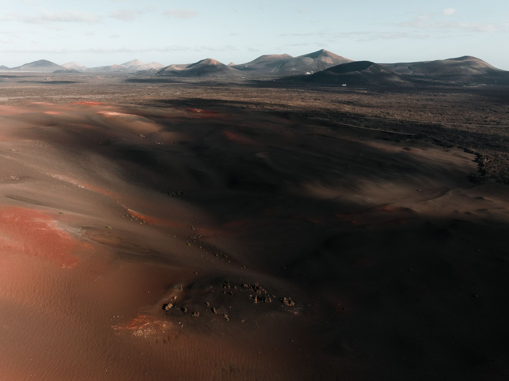 Aerial view of a volcanic landscape with dark lava fields and rolling hills under soft daylight.