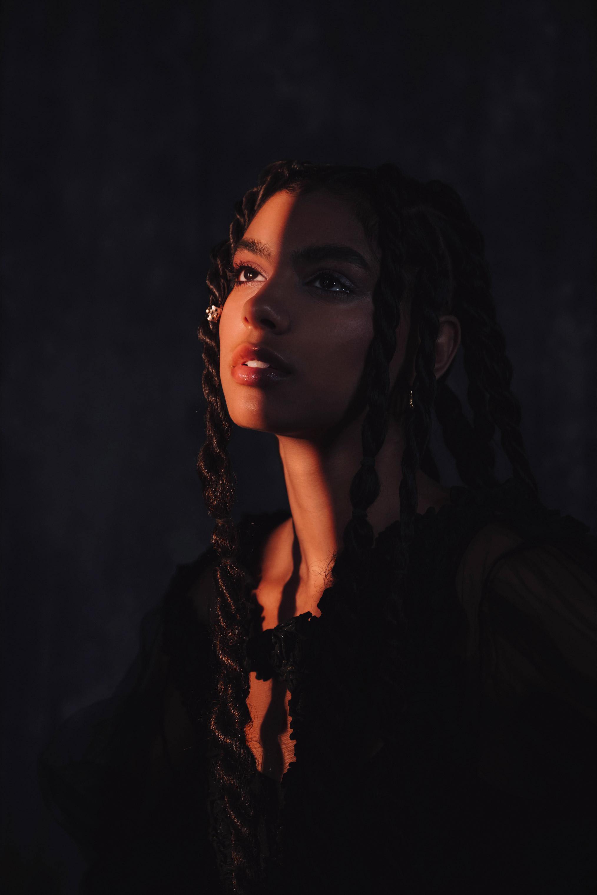 Person with braids looking up with strip of light on face, photo by Brandon Woelfel