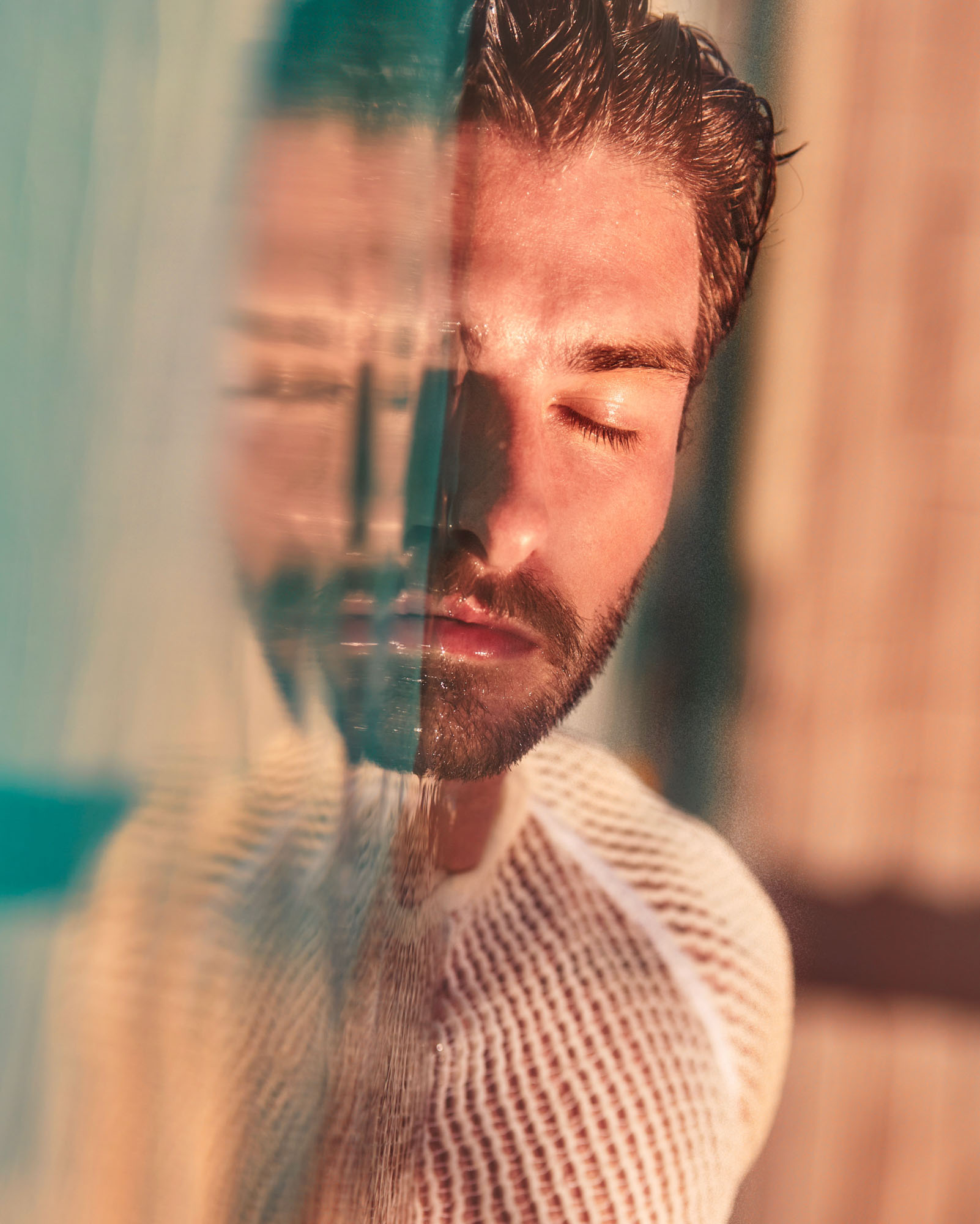 A portrait of a model with their eyes closed, half submerged in water, their face reflecting in the water, giving a sense of serenity