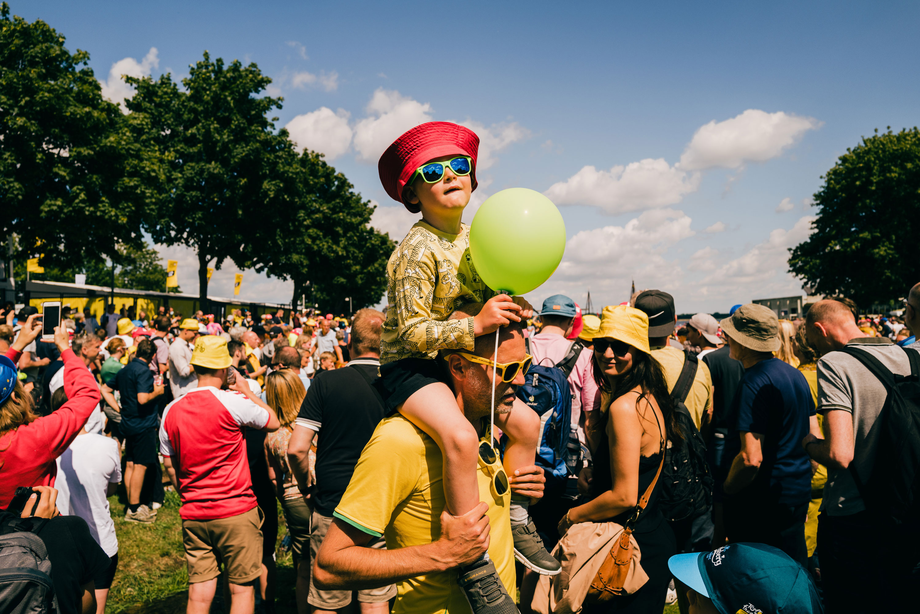 Kind auf den Schultern einer Person, das einen grünen Ballon bei der Tour De France 2022 der Frauen trägt
