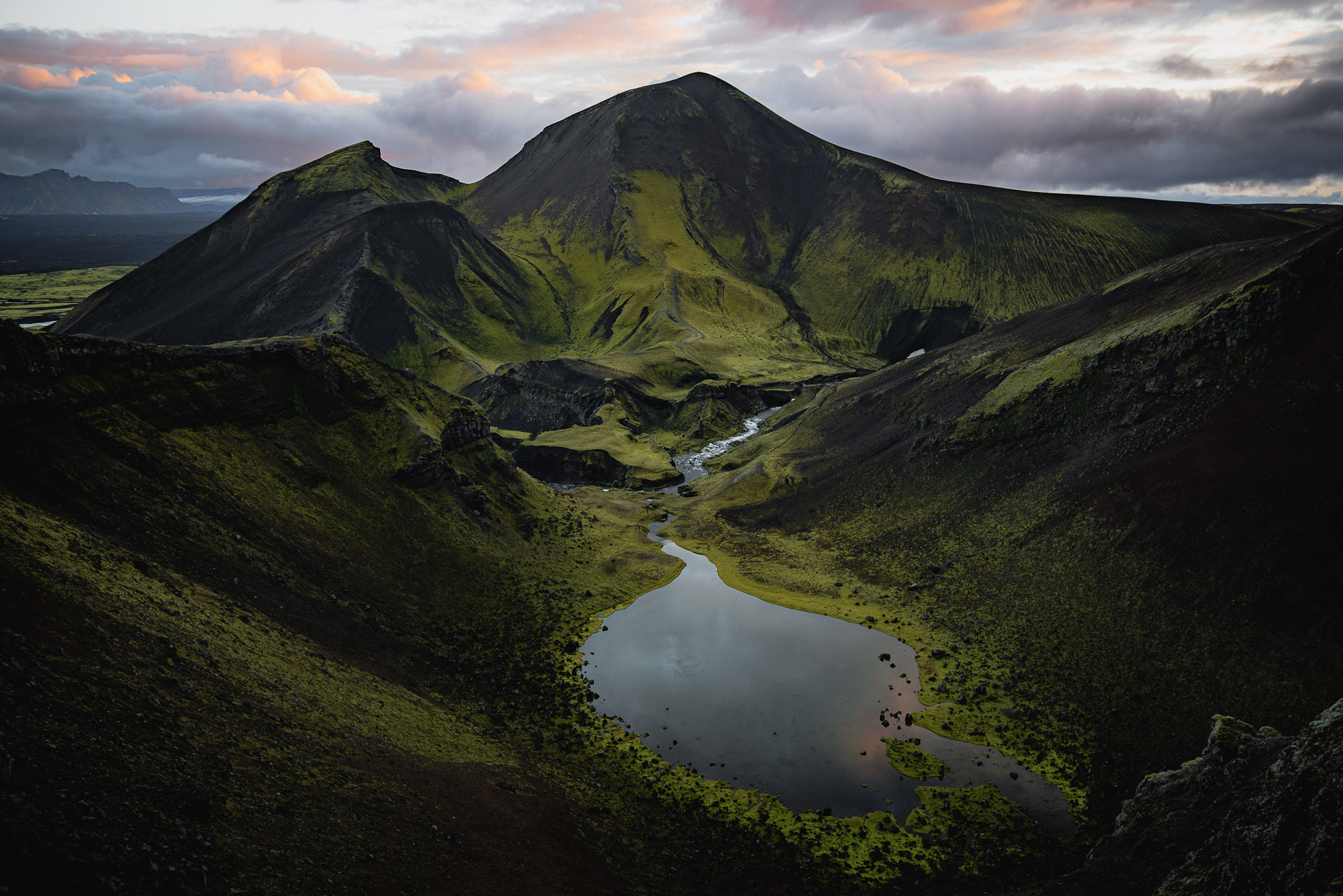 A landscape photo of a river running into a lake in Iceland, there are grass-covered hills and mountains in the background, shot by Paul with a Panasonic S1R