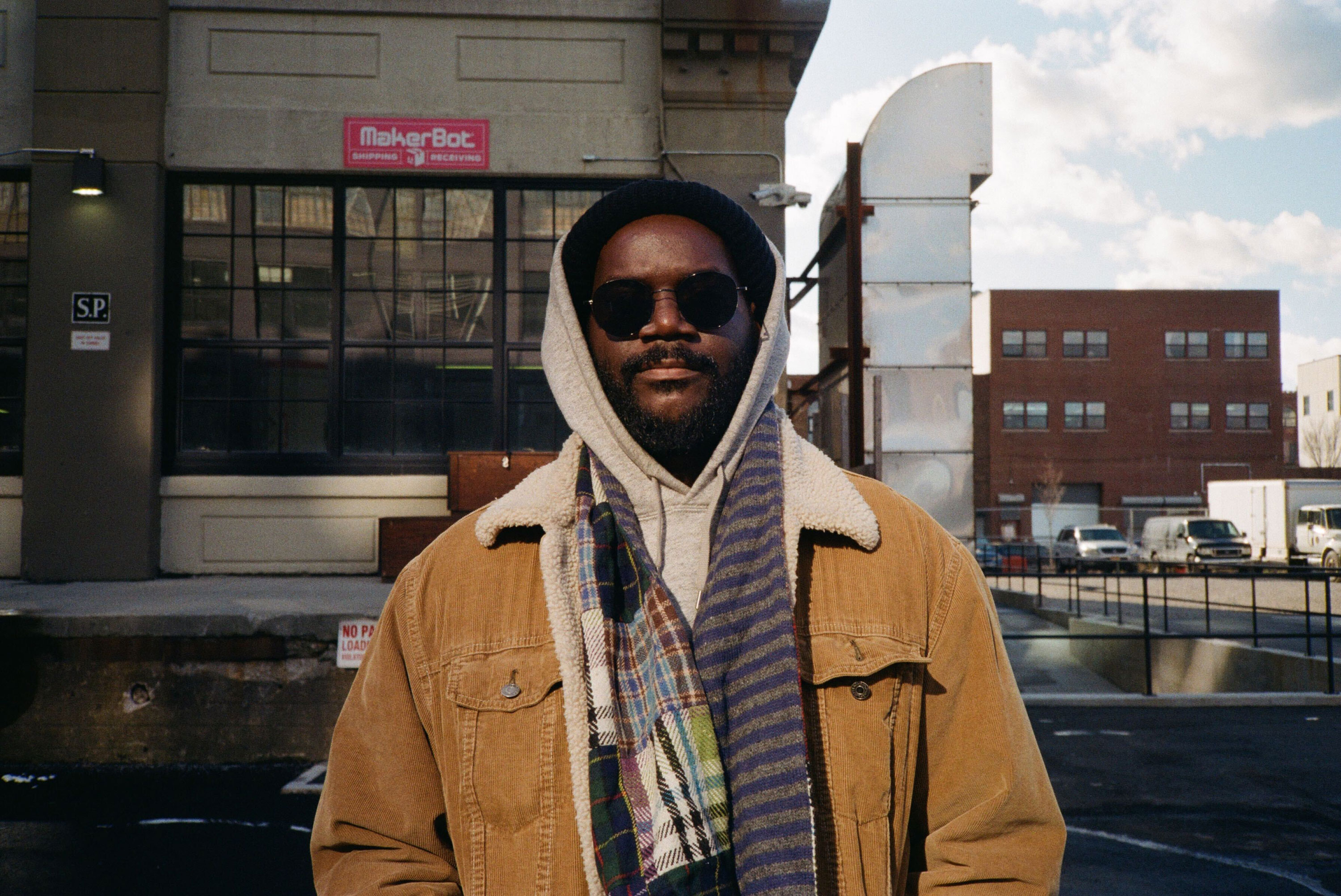 A model wearing an orange sheepskin jacket, scarf and sunglasses looks at the camera